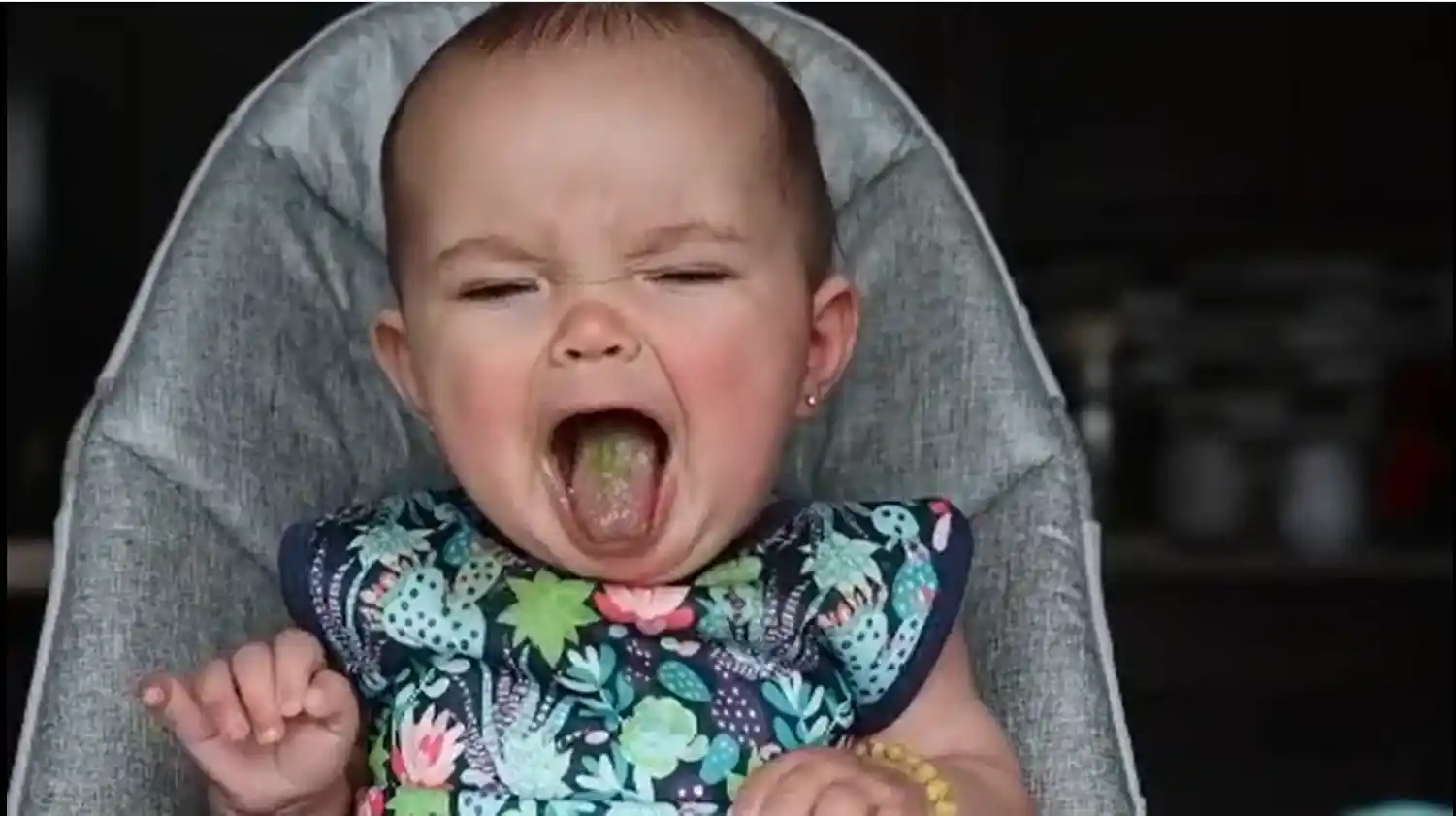 a baby in a high chair gagging with her tongue stuck out and eyes closed