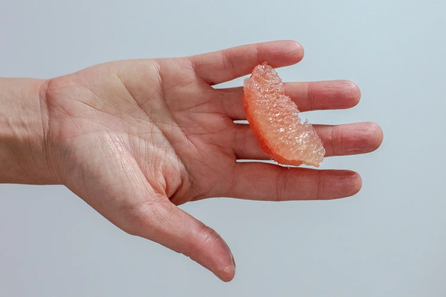a hand holding one large slice of pomelo with membrane removed for babies 6 months+