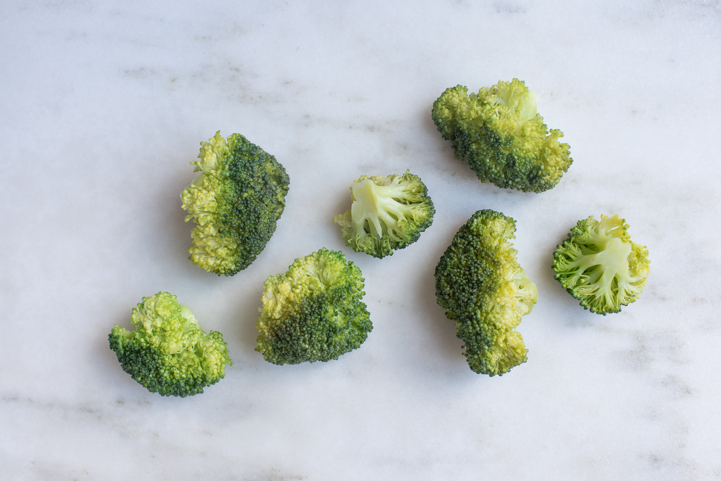 seven large cooked broccoli florets on a marble background