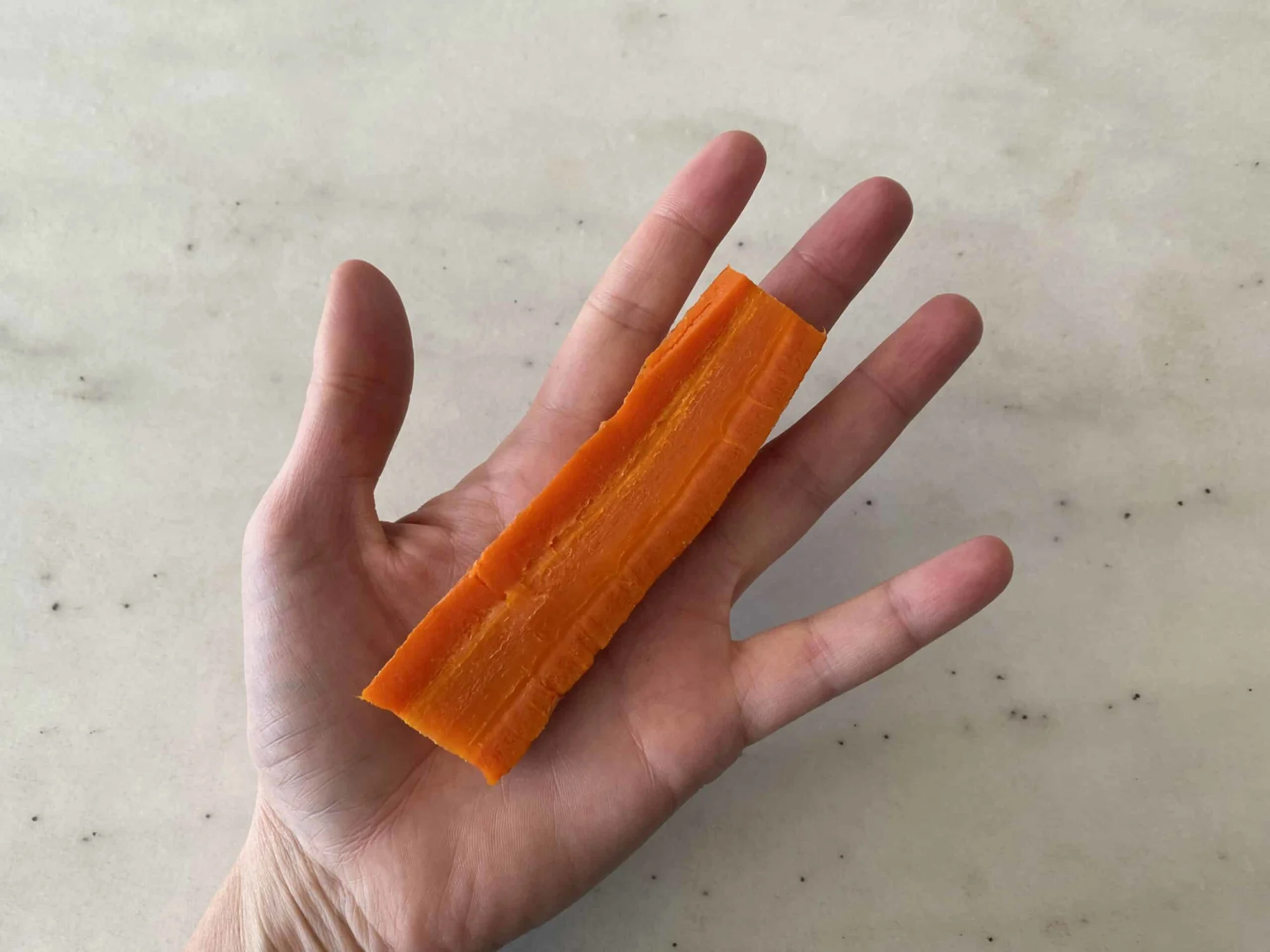 a hand holding a cooked carrot cut in half lengthwise for babies 6 months+
