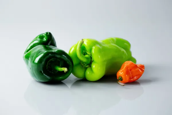 three whole chili peppers on a white background, one dark green, one light green, and one small and bright orange