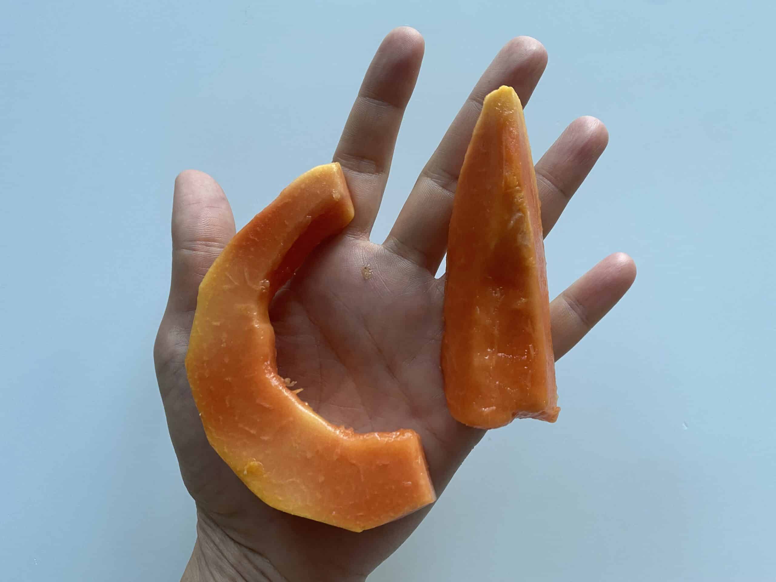a hand holding 2 ripe crescents of papaya for babies 6 months+