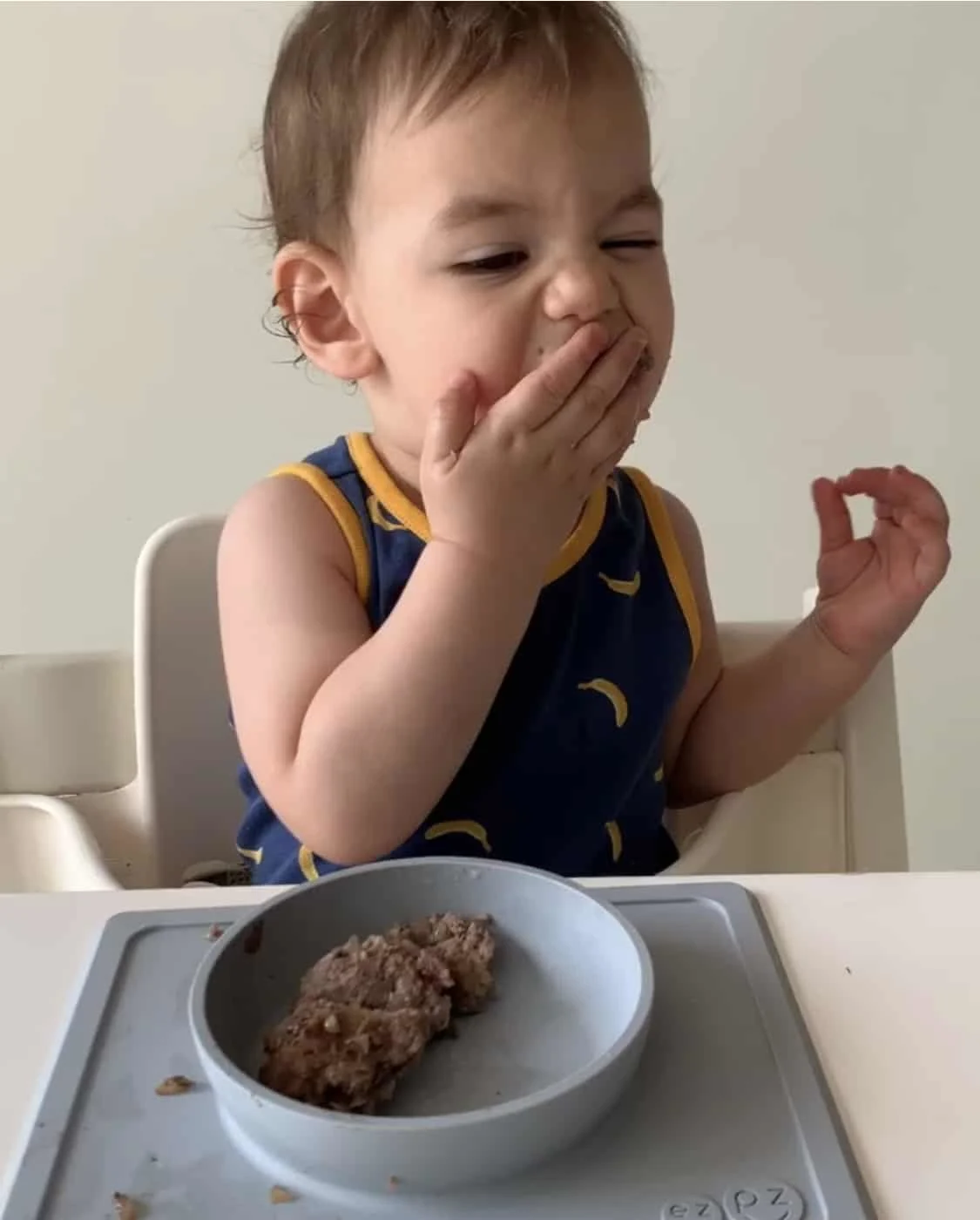 a baby boy shovels a hamburger into his mouth with starting solids