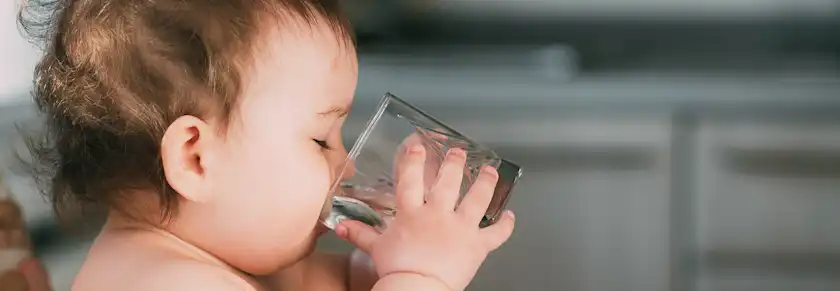 side view of a baby drinking a glass cup of water