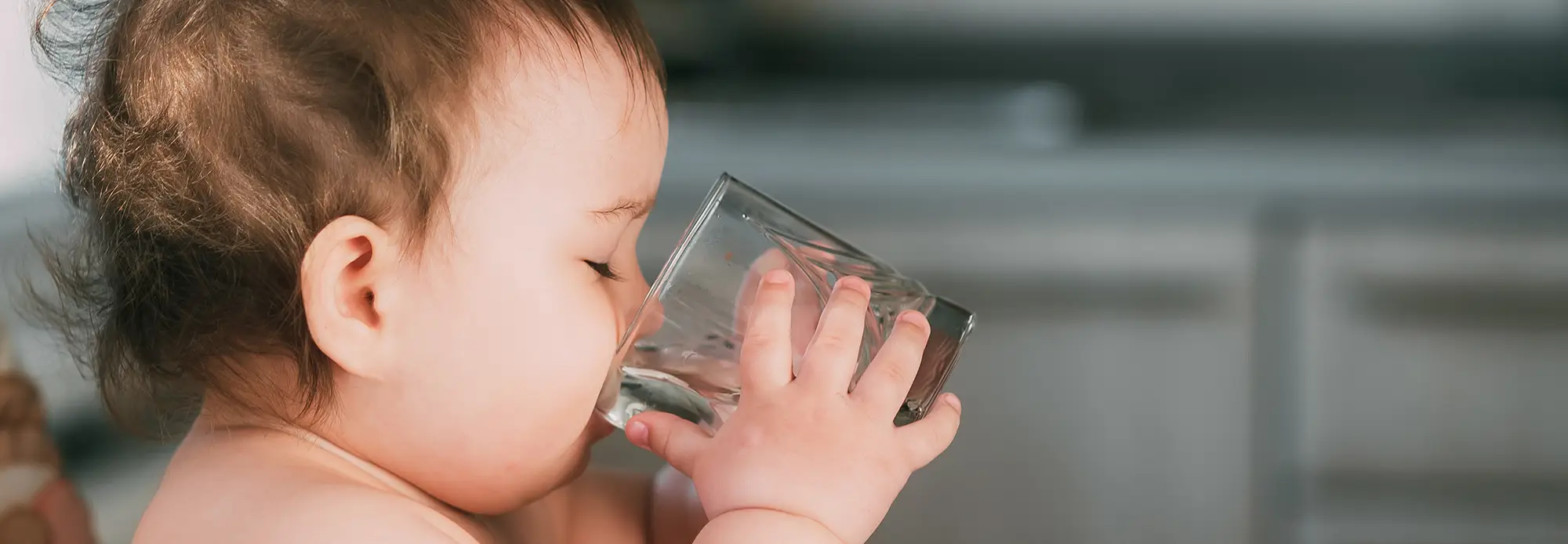 side view of a baby drinking a glass cup of water