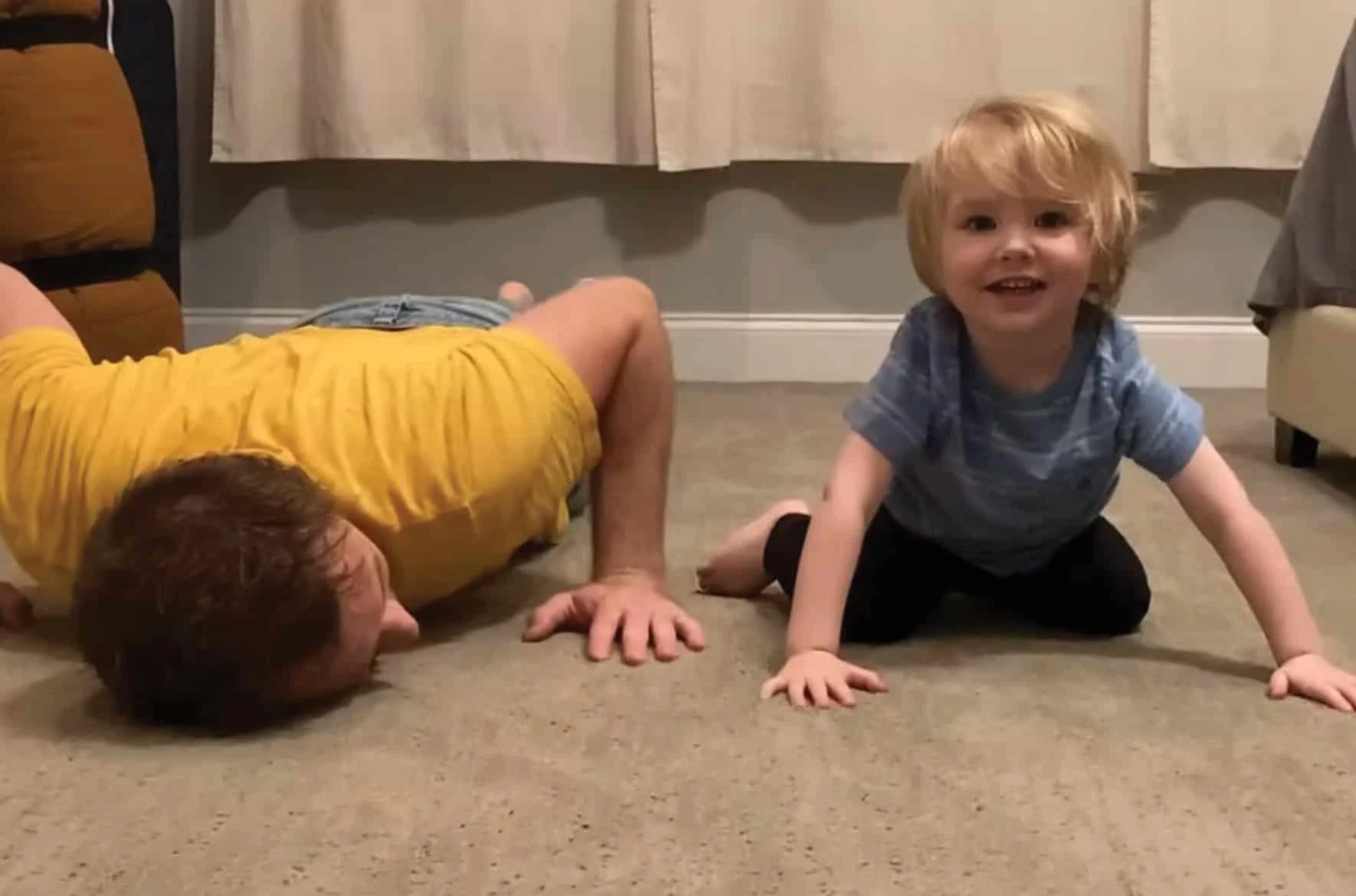 toddler sitting happily on the floor next to a man laying down playfully on the floor