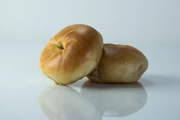 a photograph of two plain bagels, one propped up on the other, on a white background