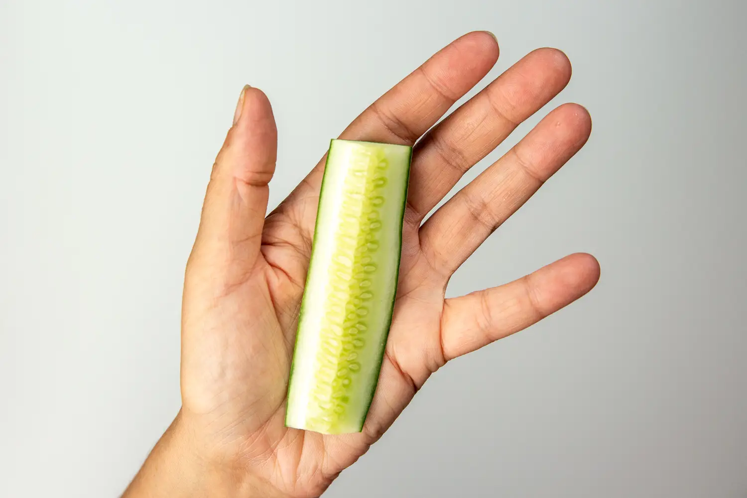 a photograph of a hand holding a long thin cucumber spear, with both tapered ends removed