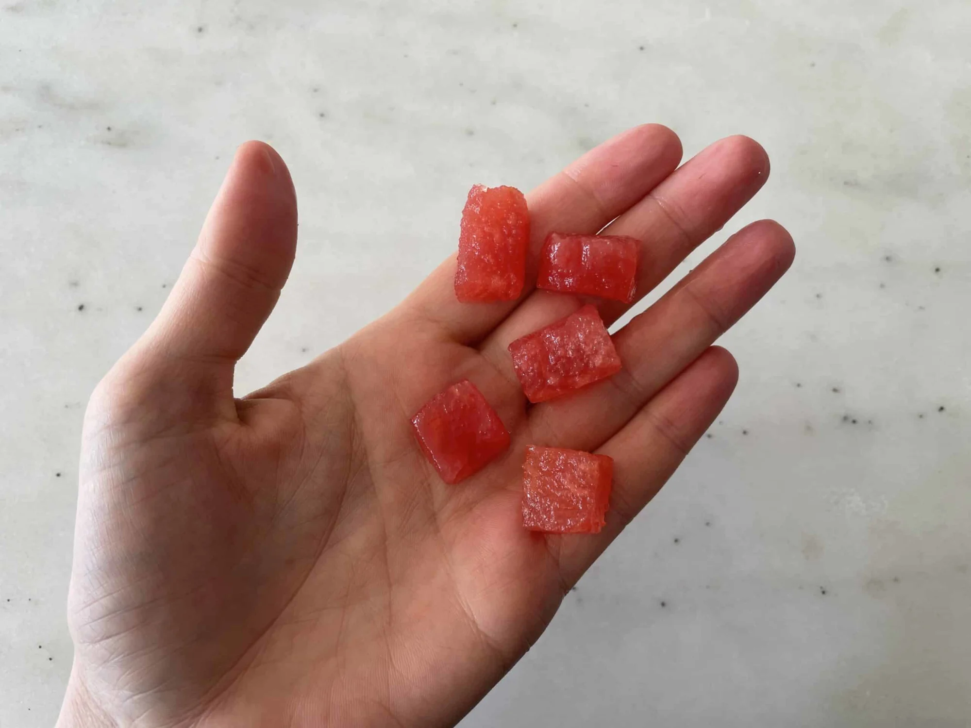 a hand holding five bite-sized pieces of watermelon for babies 9 months+