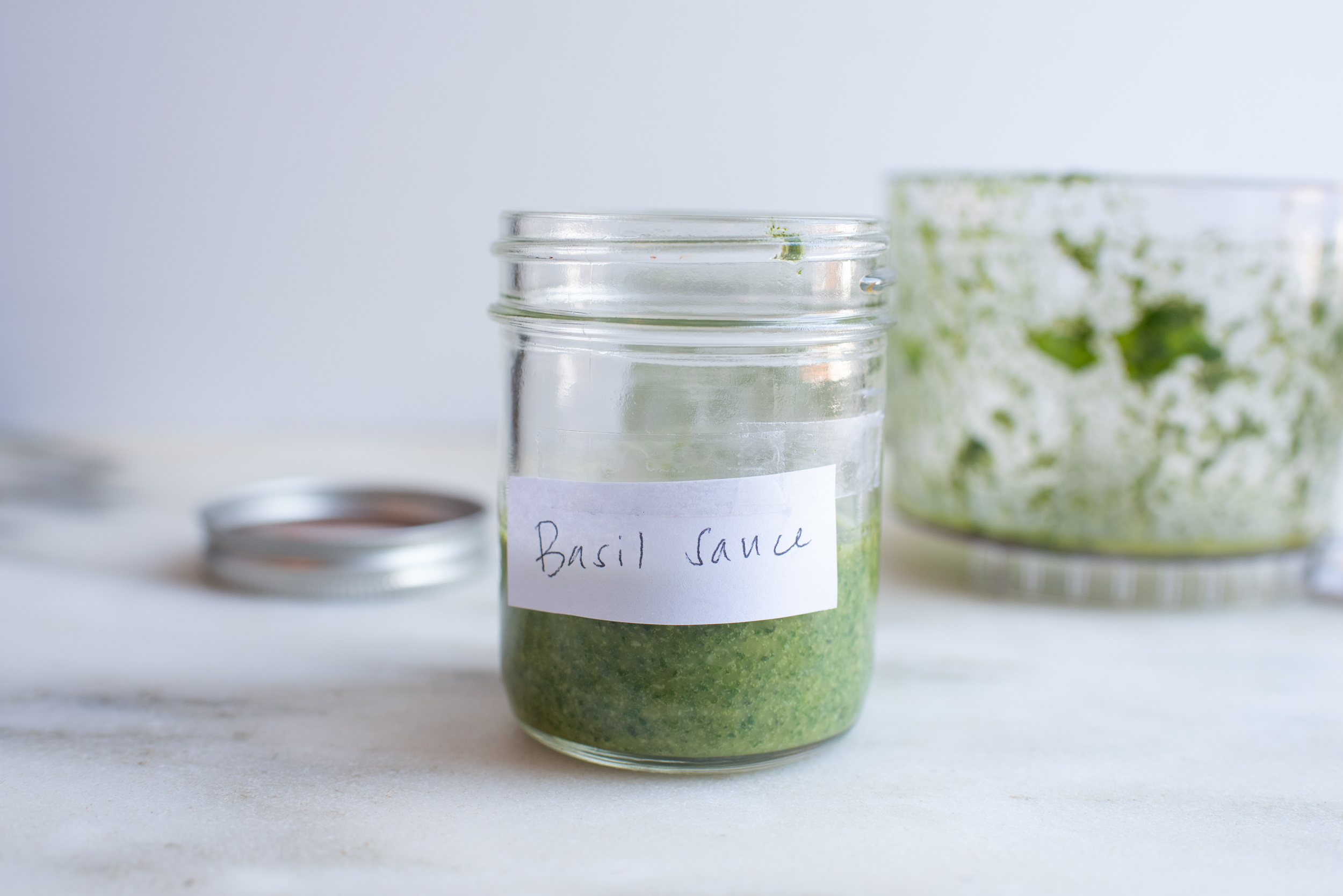 a glass jar half filled with green sauce and a label that reads "Basil Sauce"