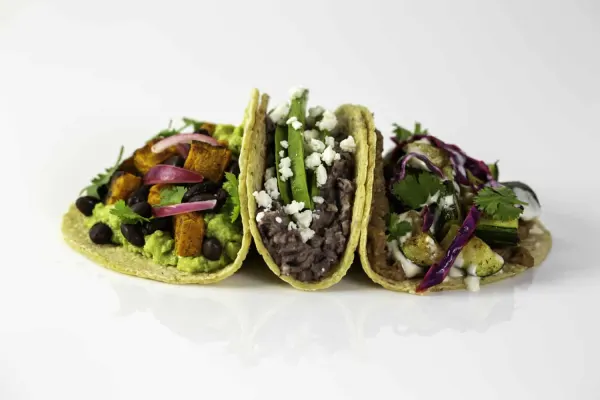 three soft tacos next to each other, one filled with avocado, black beans, and tomato, the other filled with black bean, lettuce and queso fresco, and the last with cabbage, squash, and cilantro
