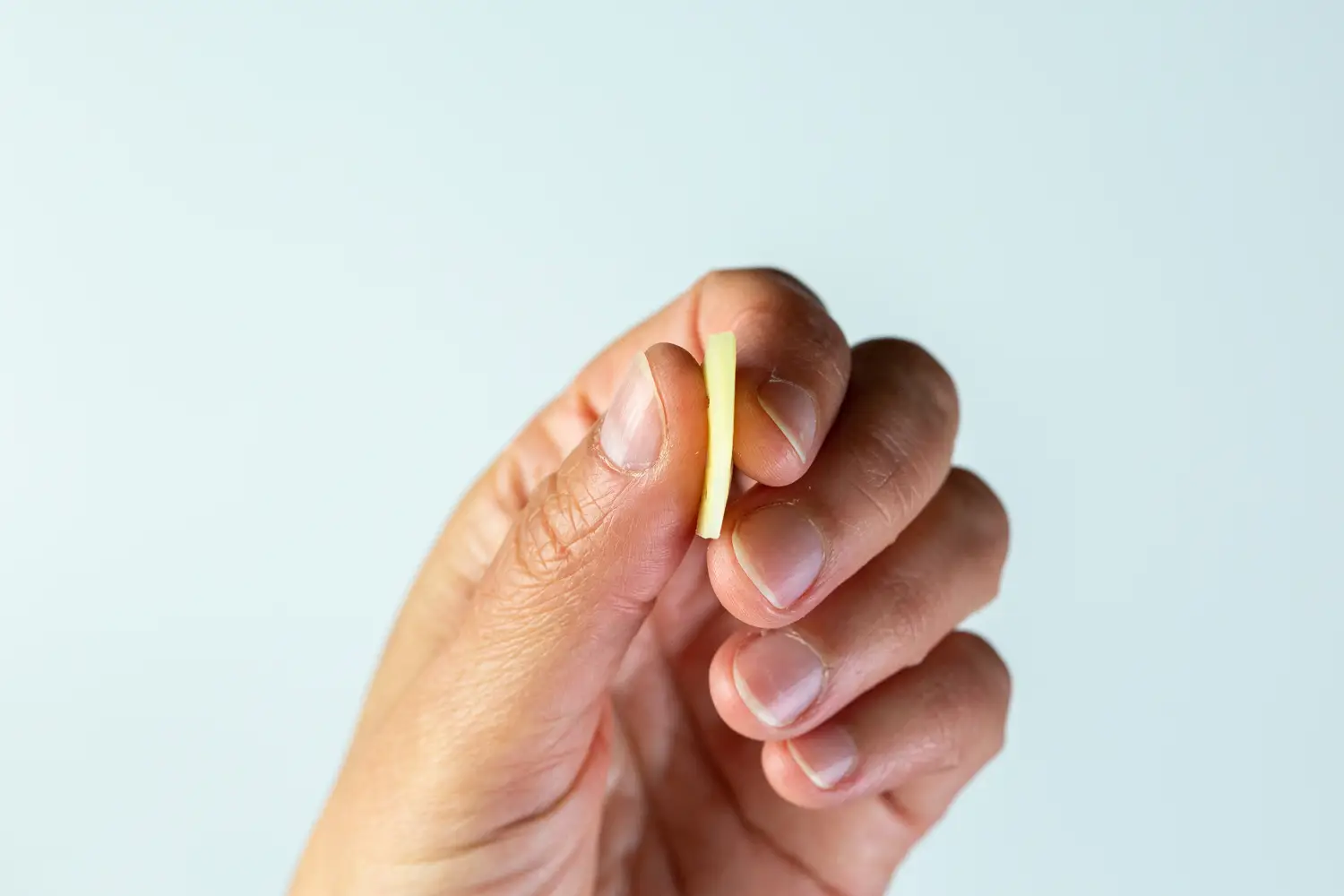 a photograph of a hand holding a small flat piece of cheese so you can see how thin it is