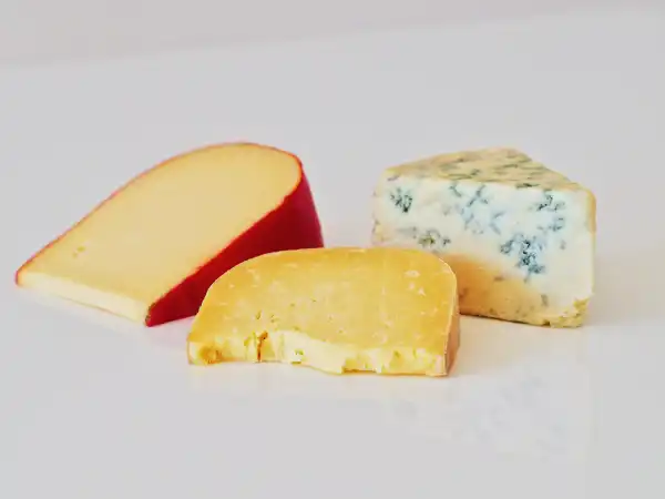 a photograph of three large wedges of different kinds of cheese on a white background