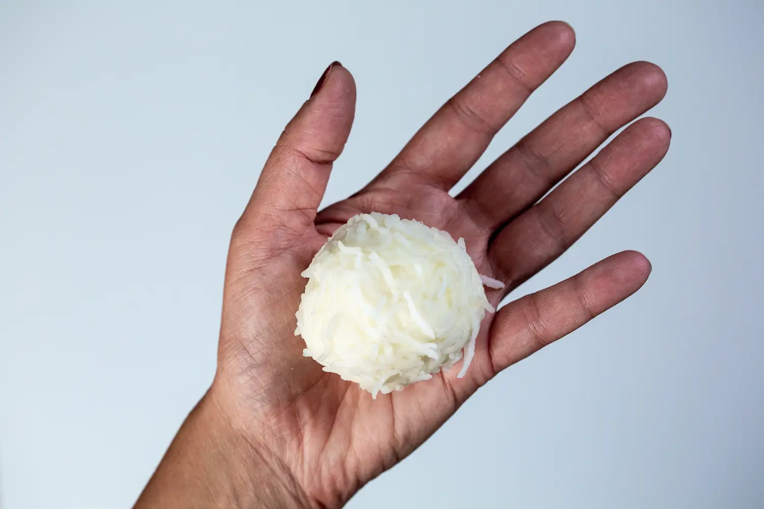 a hand holding a large, soft ball of cooked rice