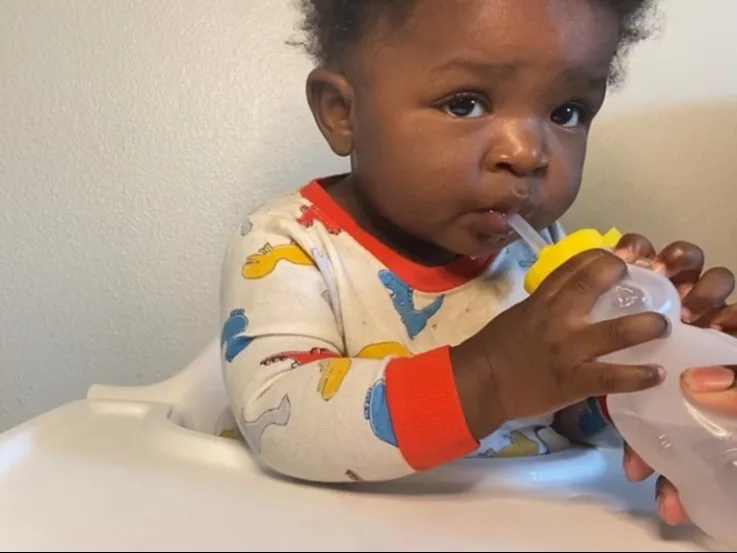 a photograph of a baby drinking from a honey bear straw trainer cup