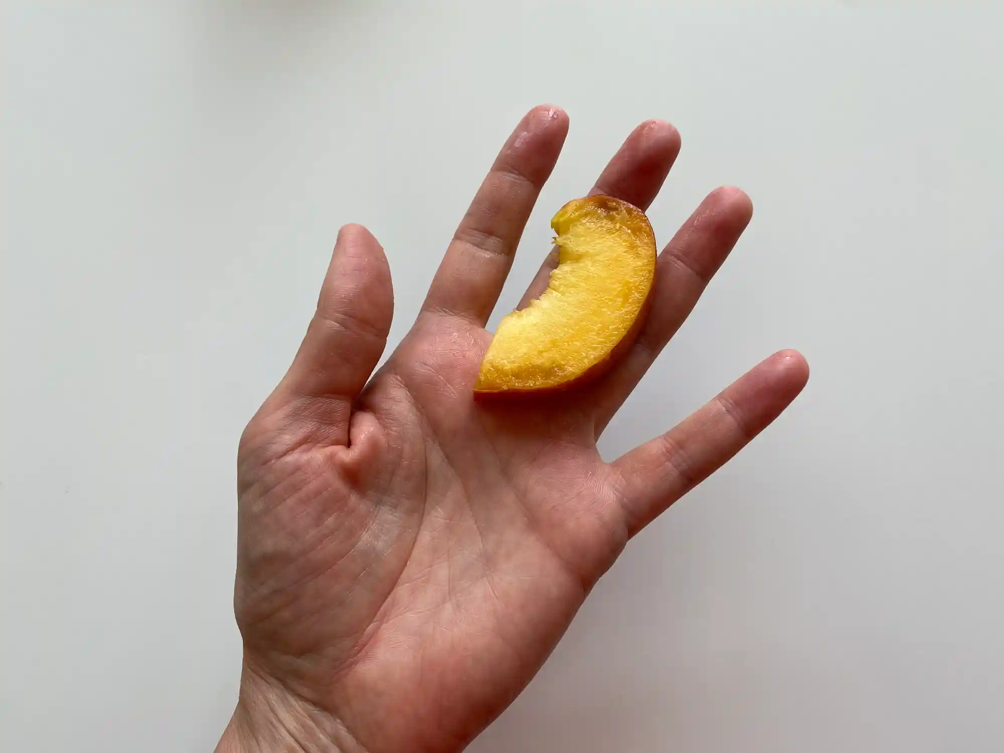 a photograph of a hand holding a thin slice of peach