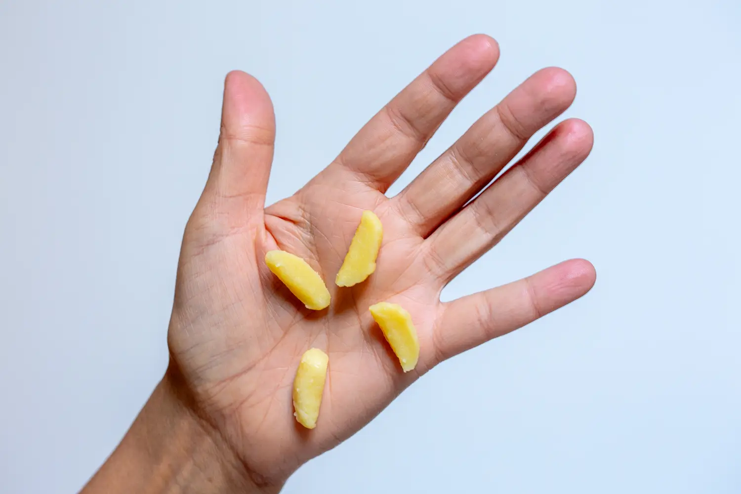 a hand holding four pieces of gnocchi quartered lengthwise