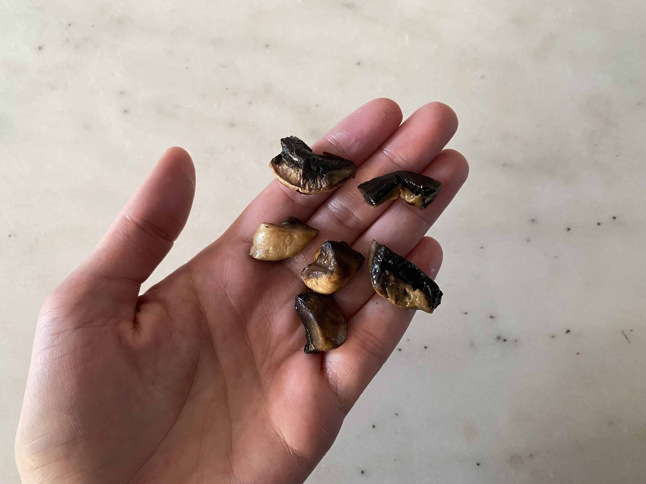 a hand holding six bite-sized pieces of cooked button mushrooms for babies starting solids