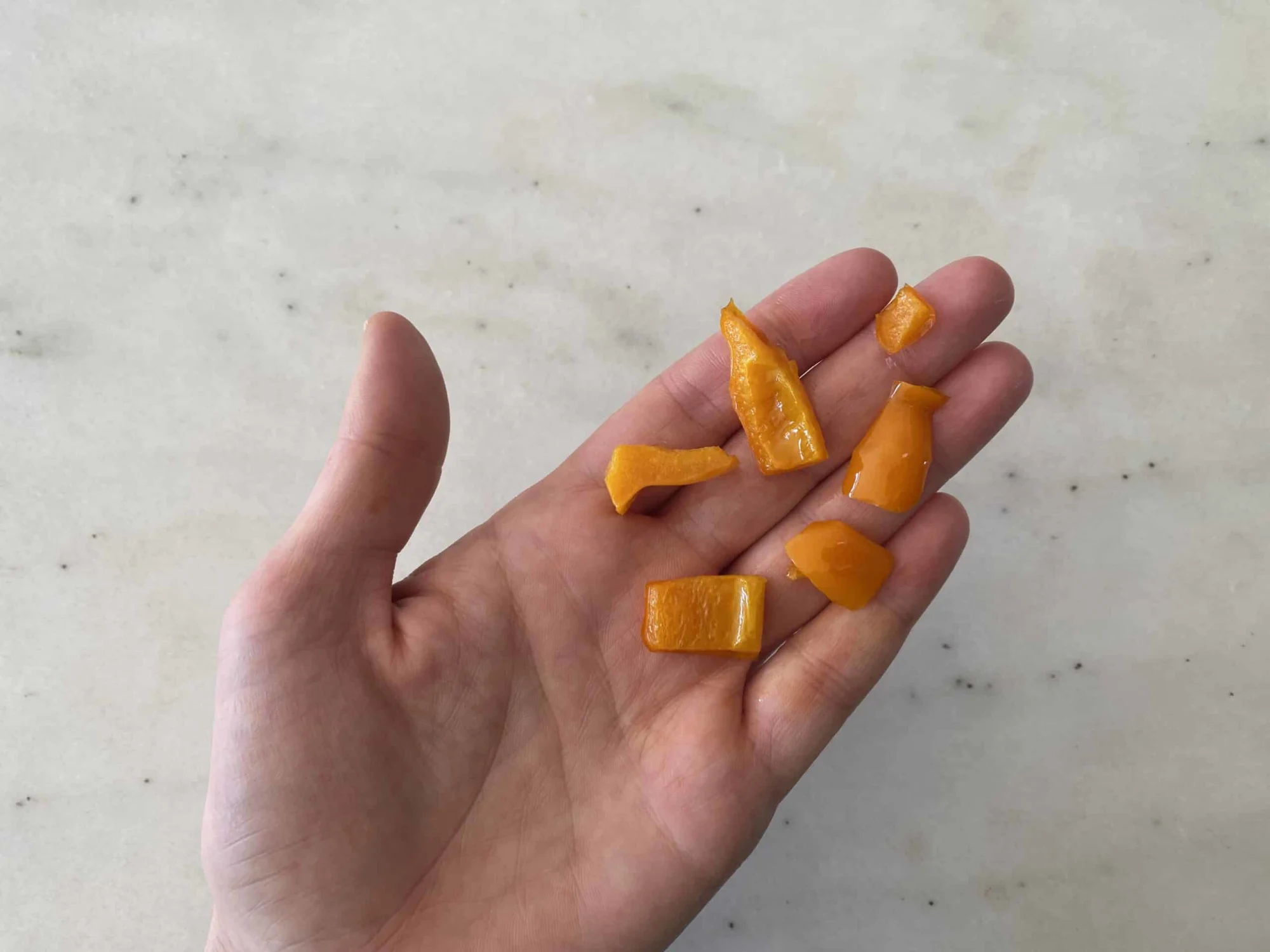 a hand holding five cooked bite-sized pieces of pepper