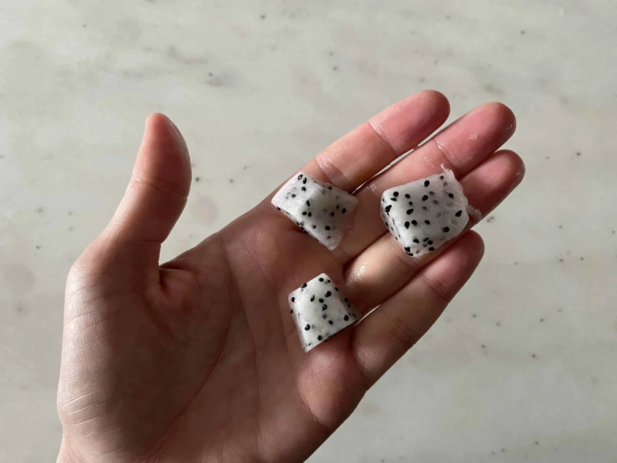 a hand holding bite-sized pieces of dragon fruit for babies 9 months+