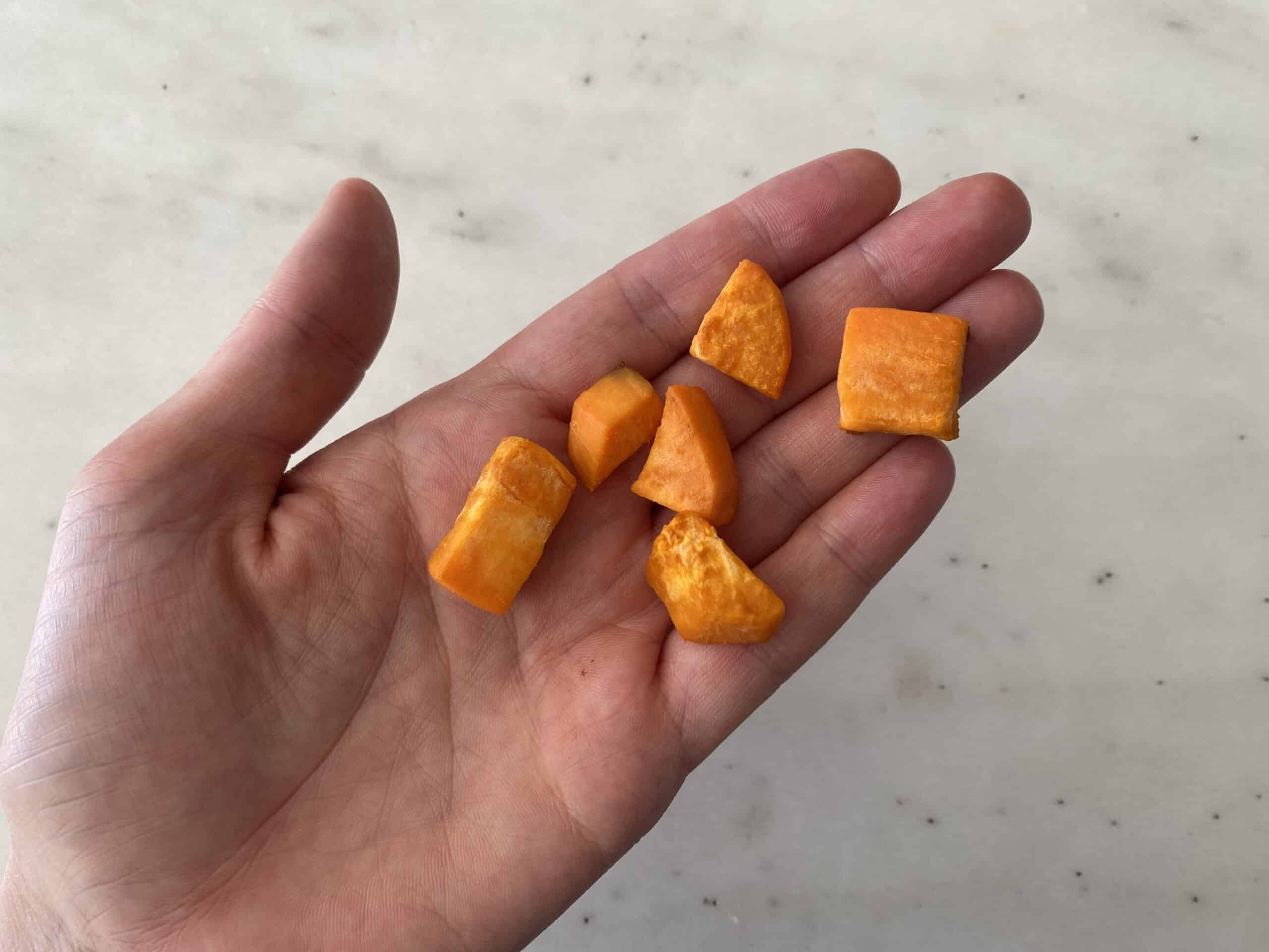 a hand holding bite-sized cooked pieces of sweet potato for babies 9 months+