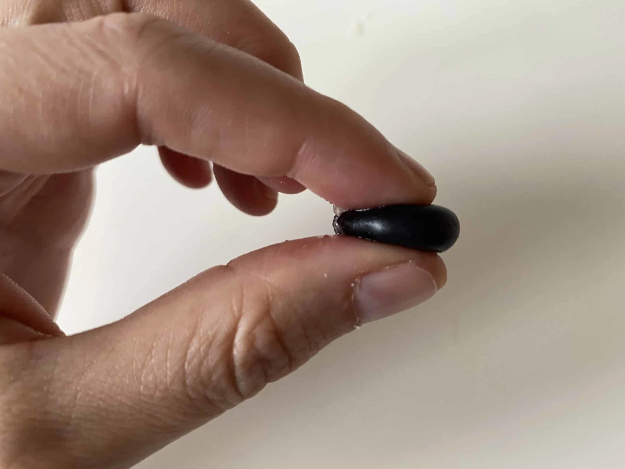 blueberry being squeezed gently between an index finger and thumb in order to flatten it