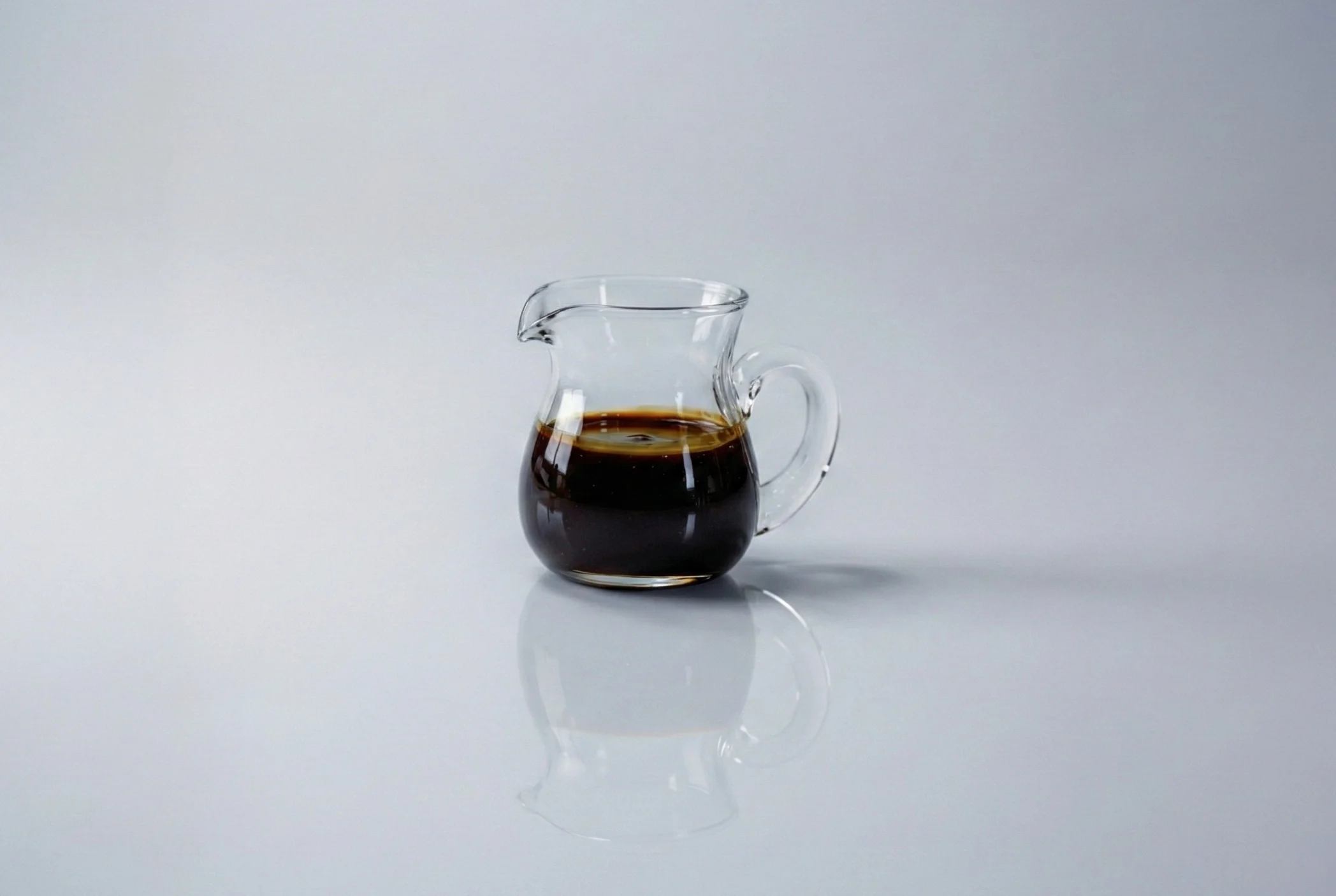 a photograph of a small glass pitcher of molasses on a white background