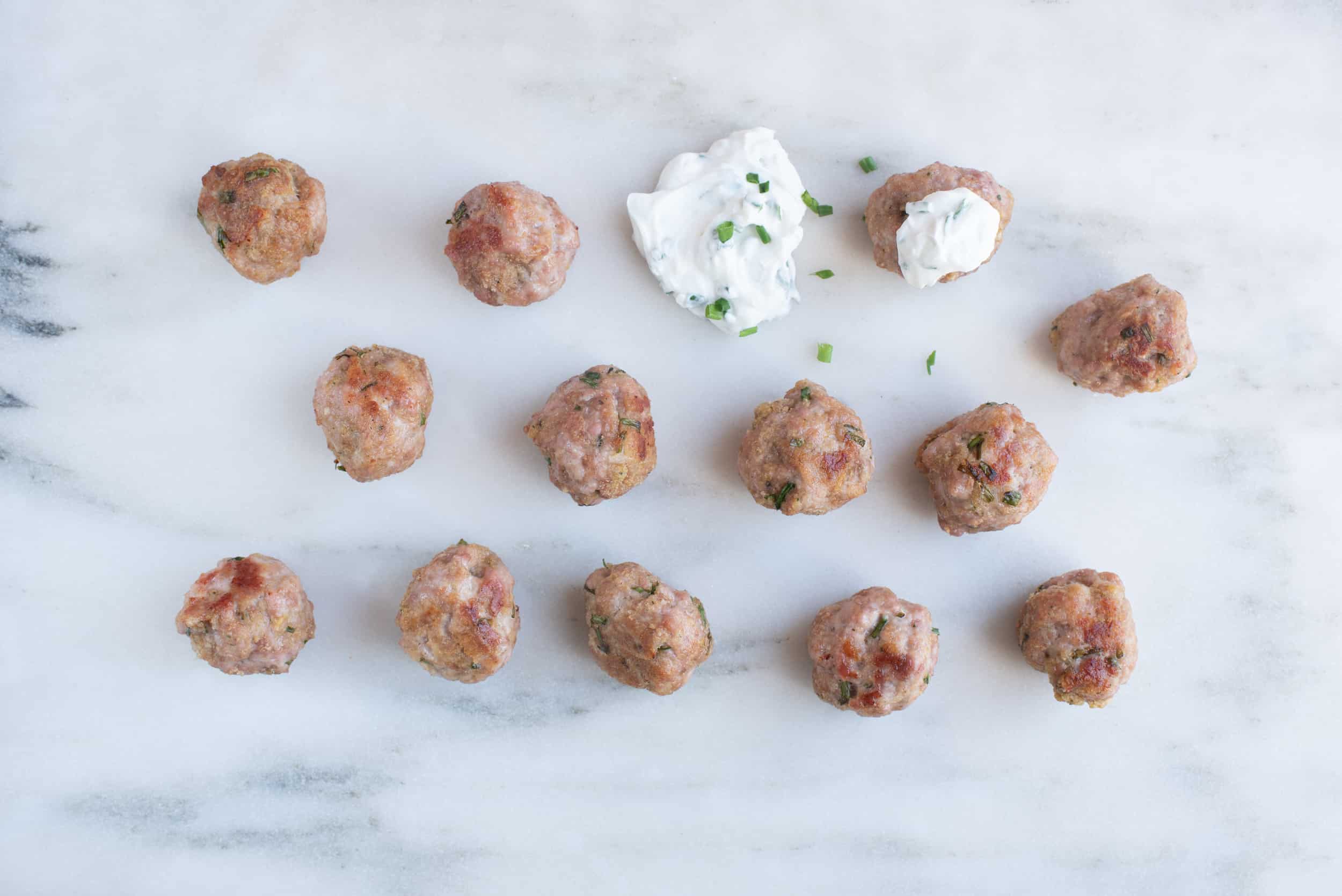 fourteen small round meatballs, a few sprinkled with chopped green chives and two topped with yogurt