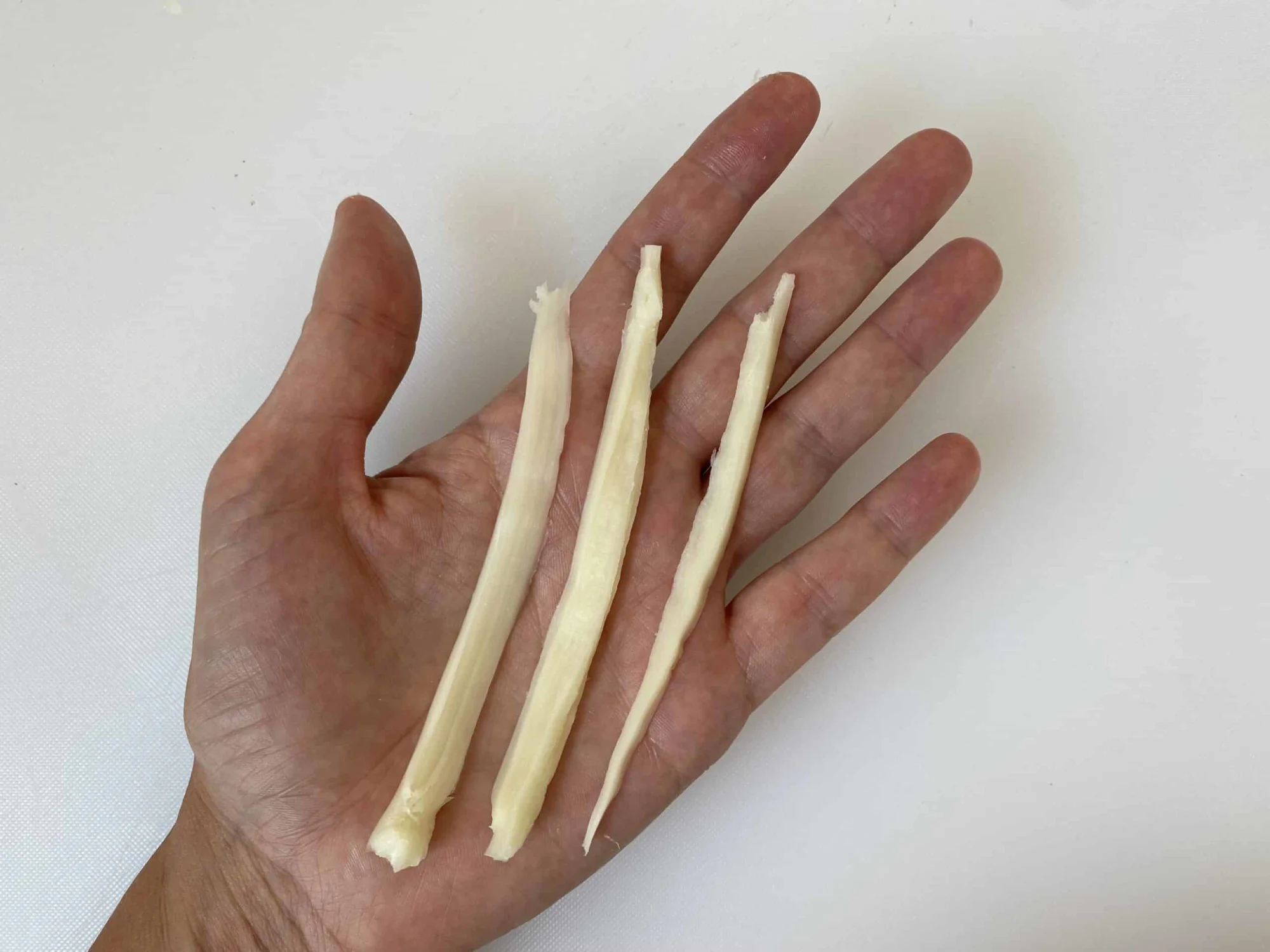 a hand holding three long, thin strands of string cheese