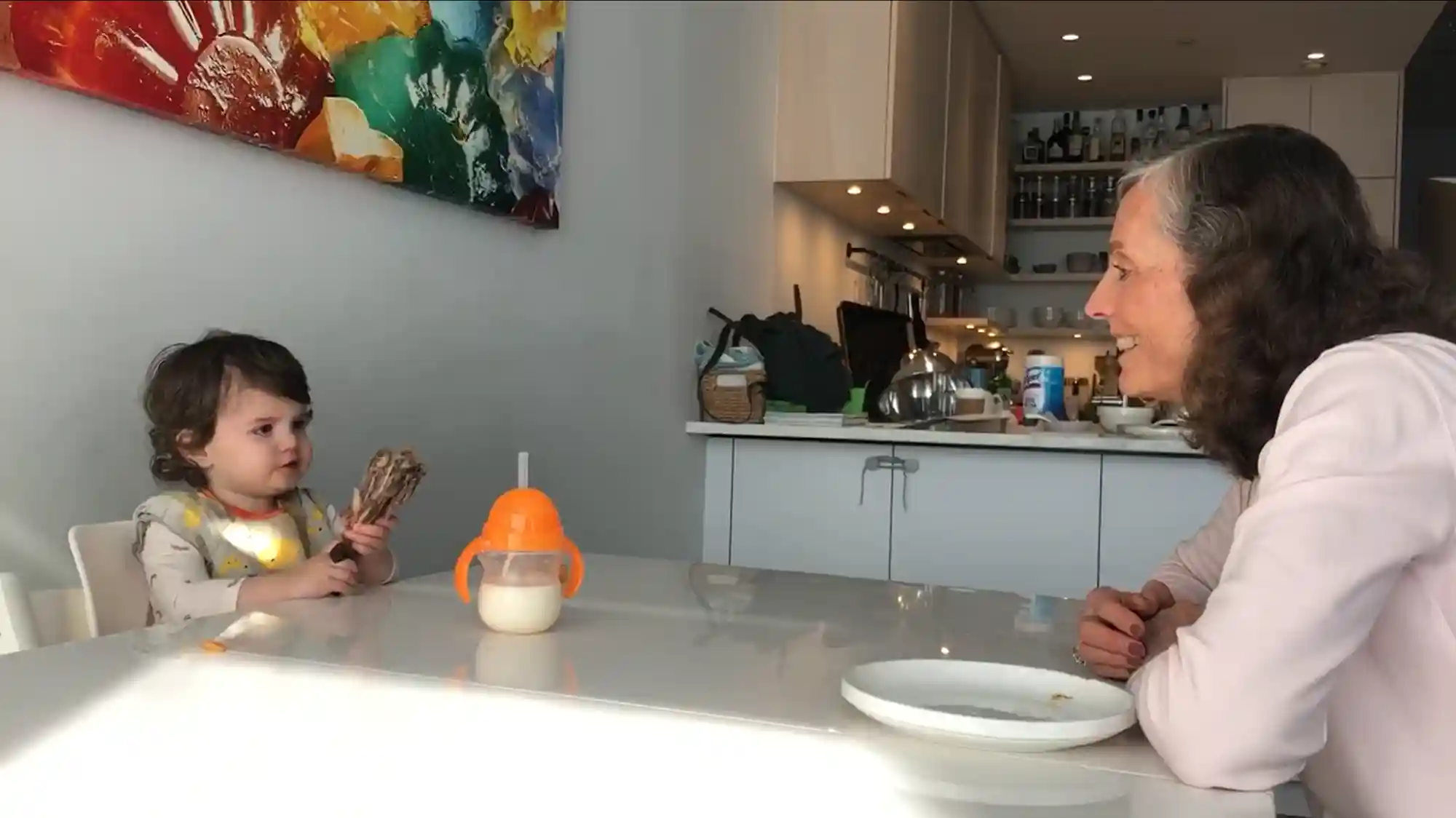a photograph of a baby and her grandmother at a table, each with a chicken drumstick
