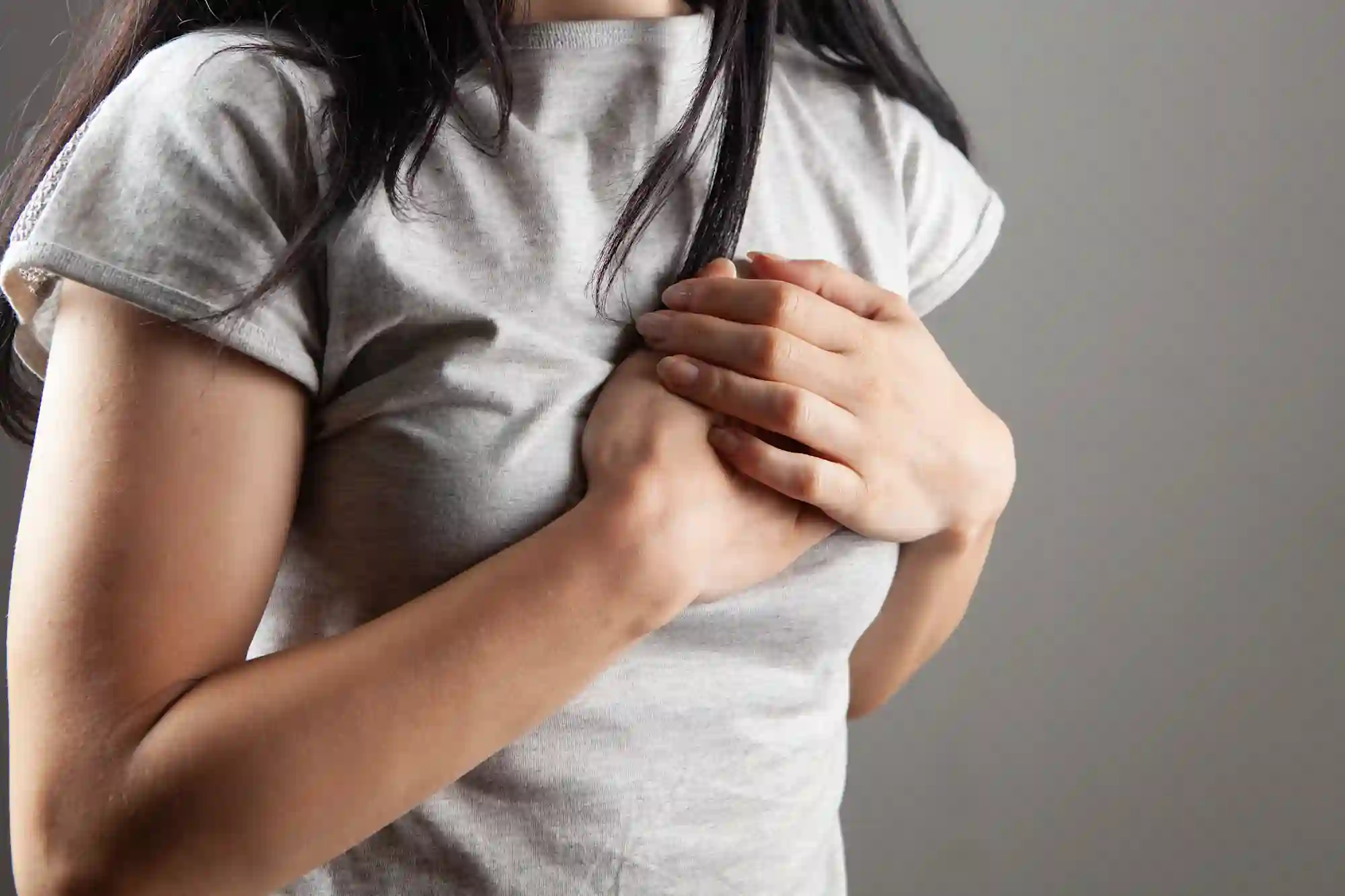 a photograph of a woman's torso, with her hands brought to her breast as if in pain