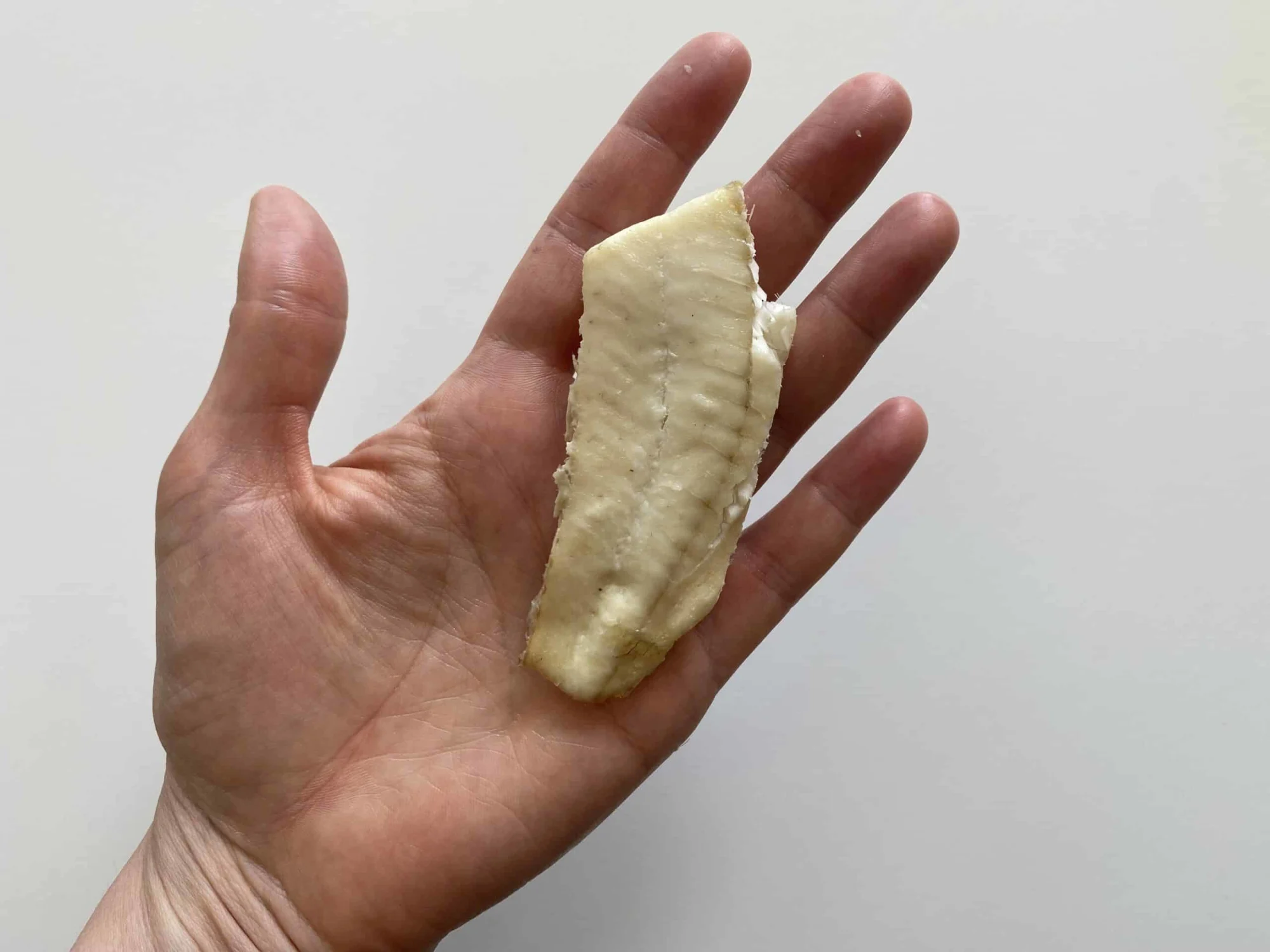 a hand holding a strip of cooked deboned sole for babies 6 months+