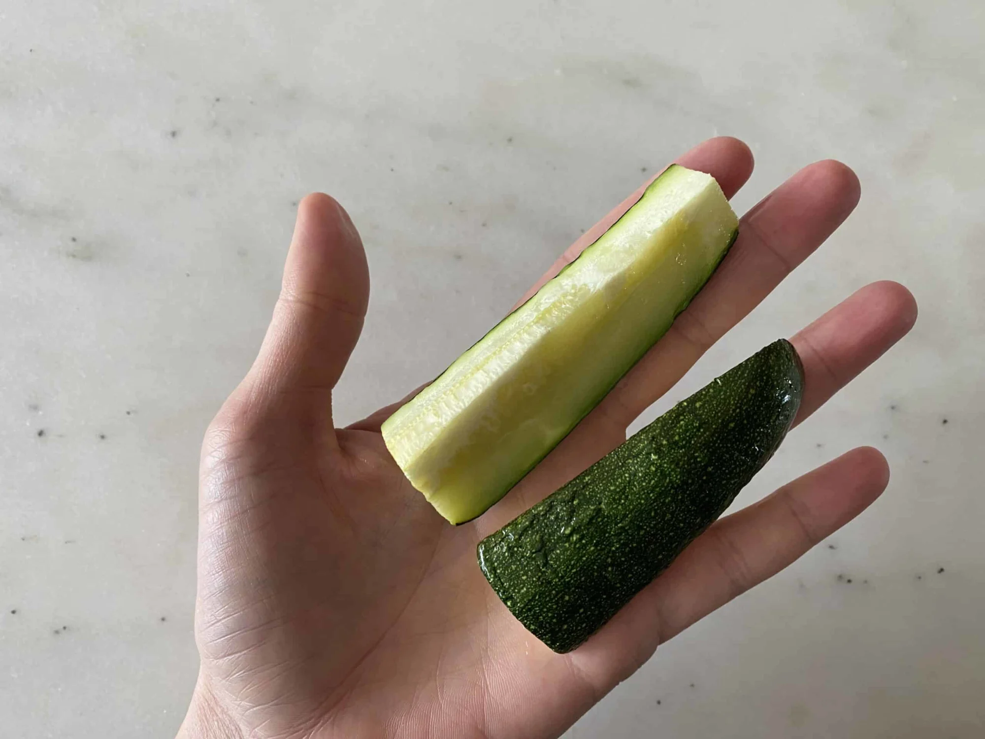 a hand holding two cooked, soft zucchini spears for babies starting solids