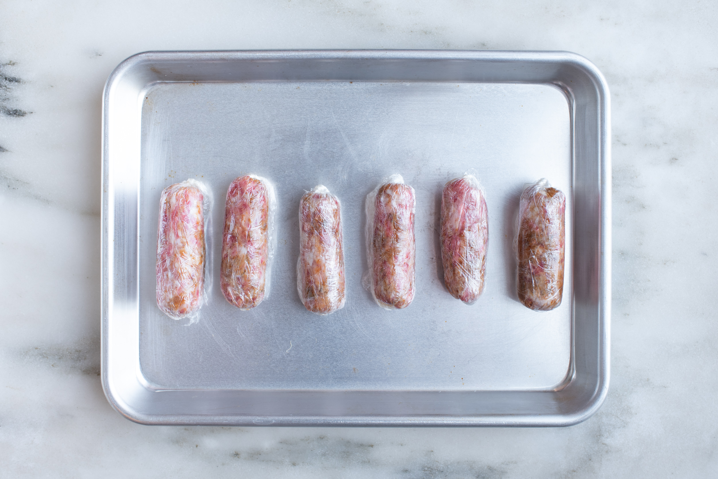 a metal sheet pan with six homemade sausages on it 