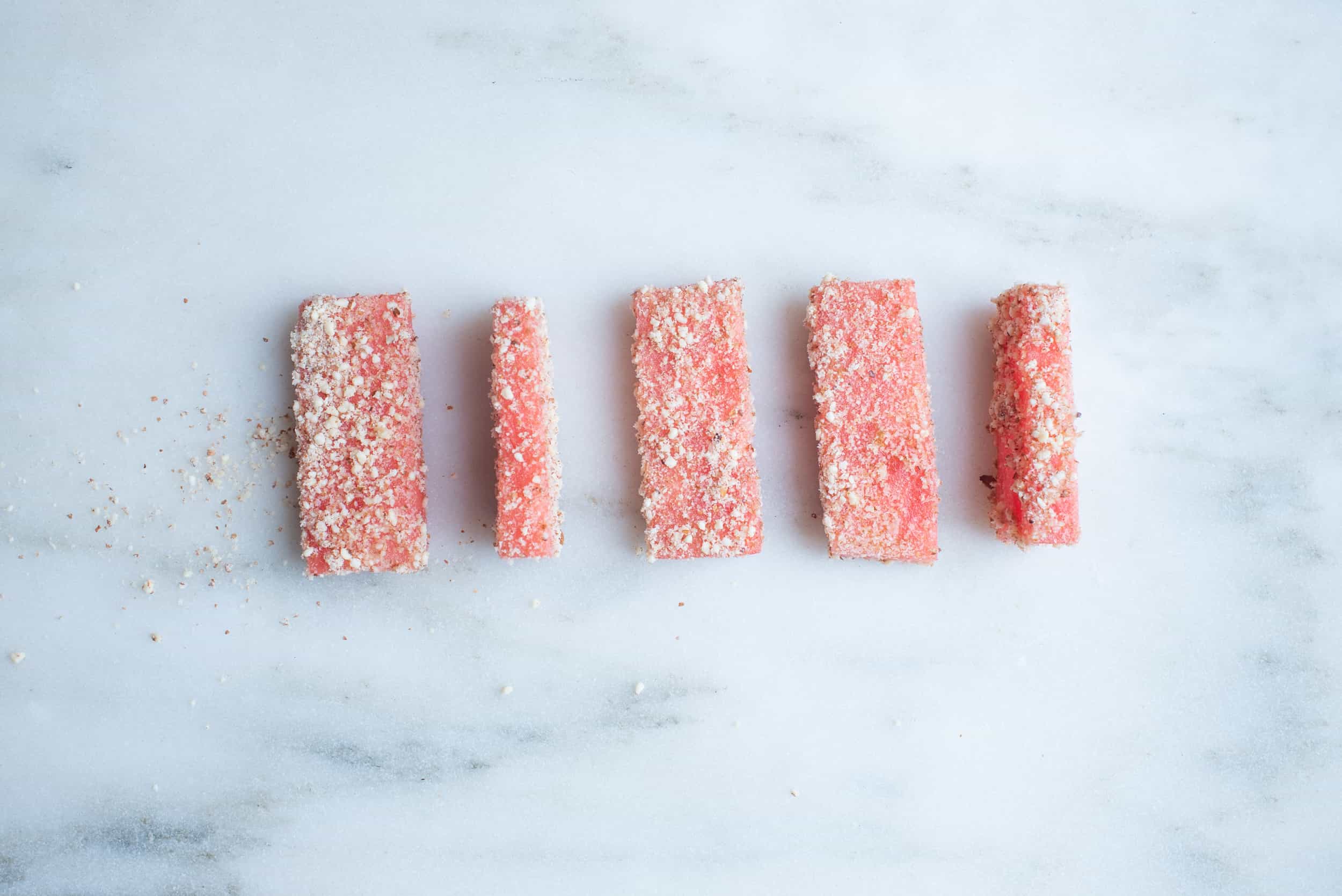 five thin rectangles of watermelon dusted with ground nut on a white background