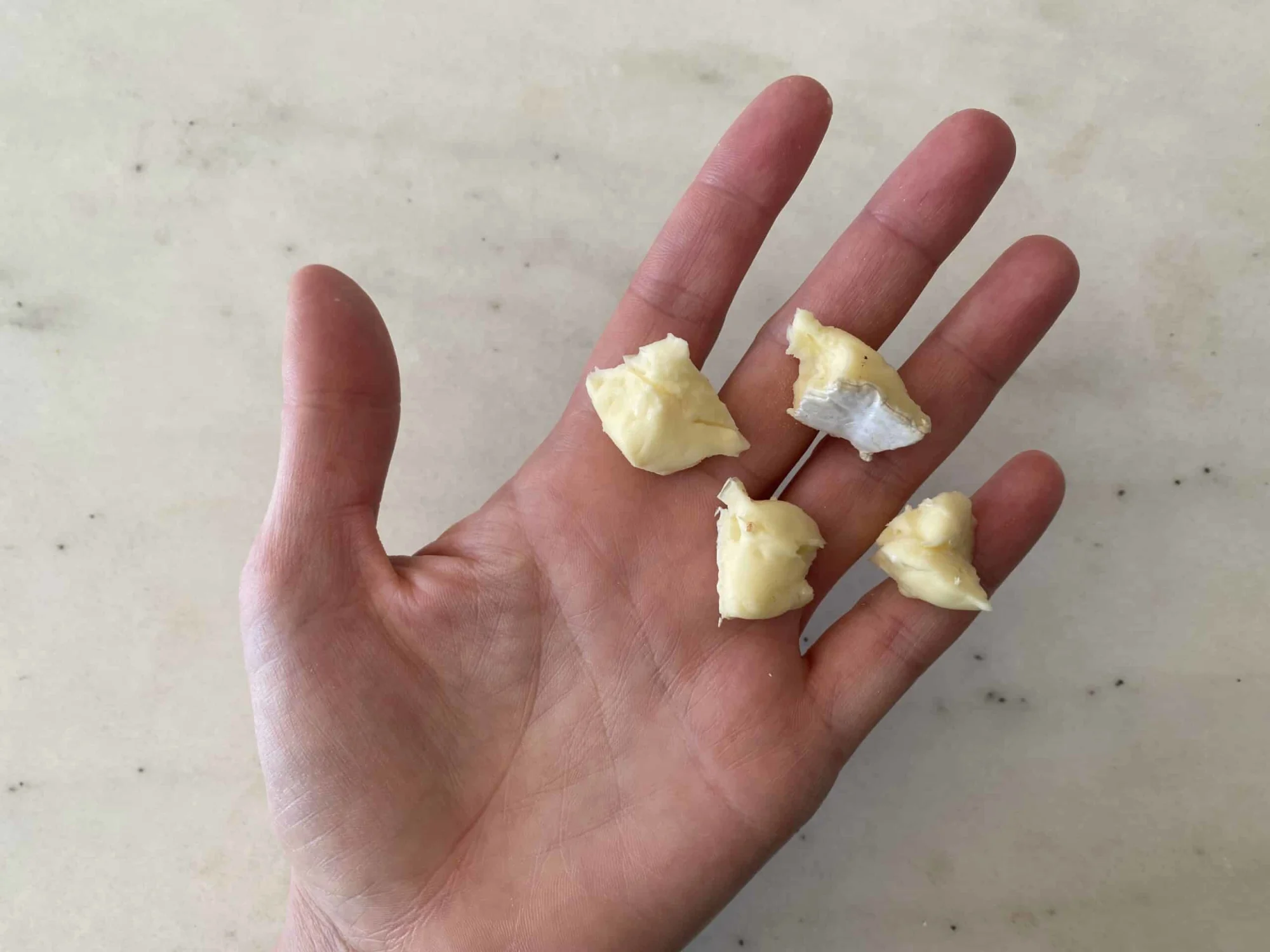 a hand holding four bite-sized pieces of camembert