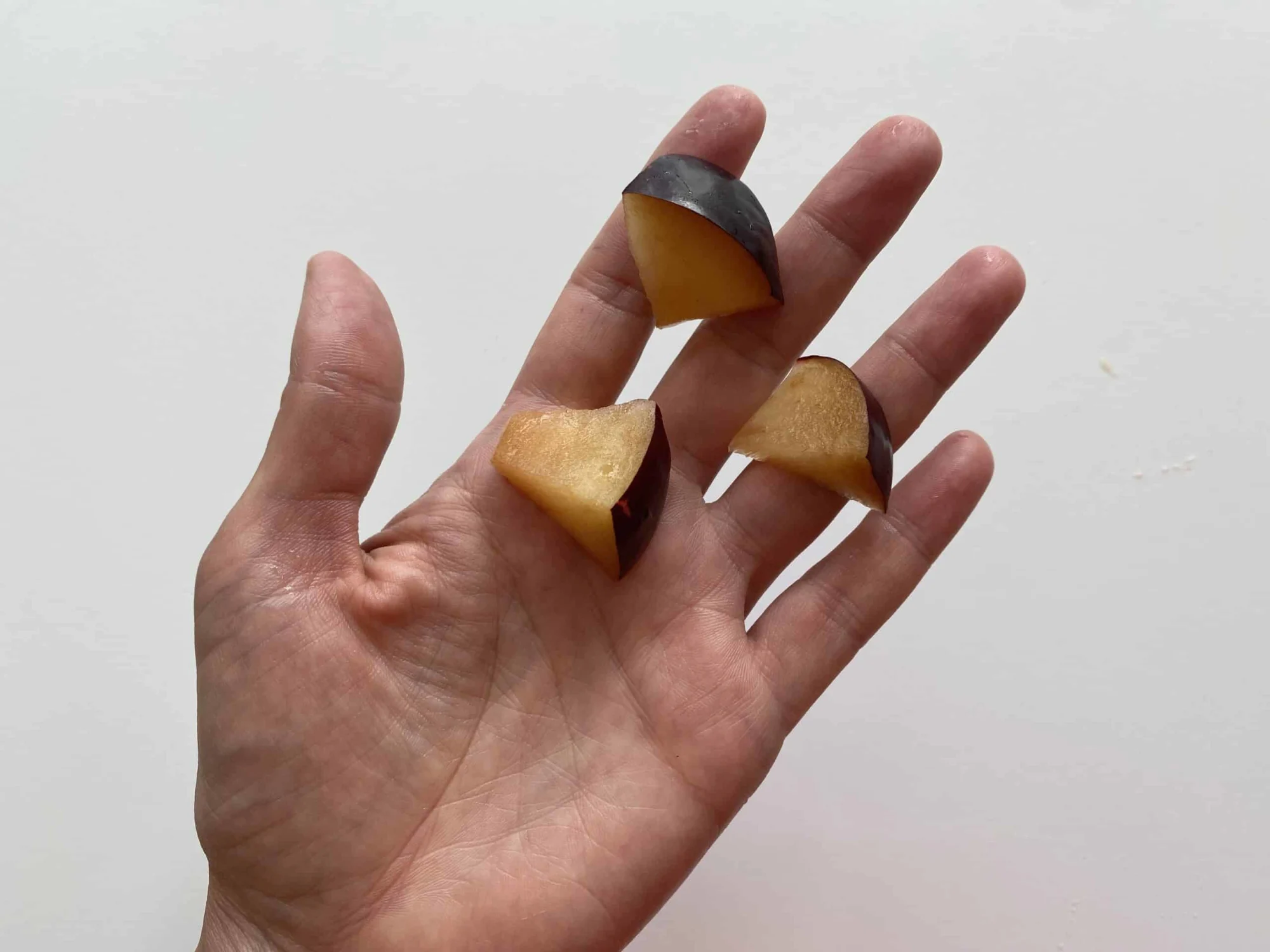 a hand holding 3 bite size pieces of plum for babies 12 months+