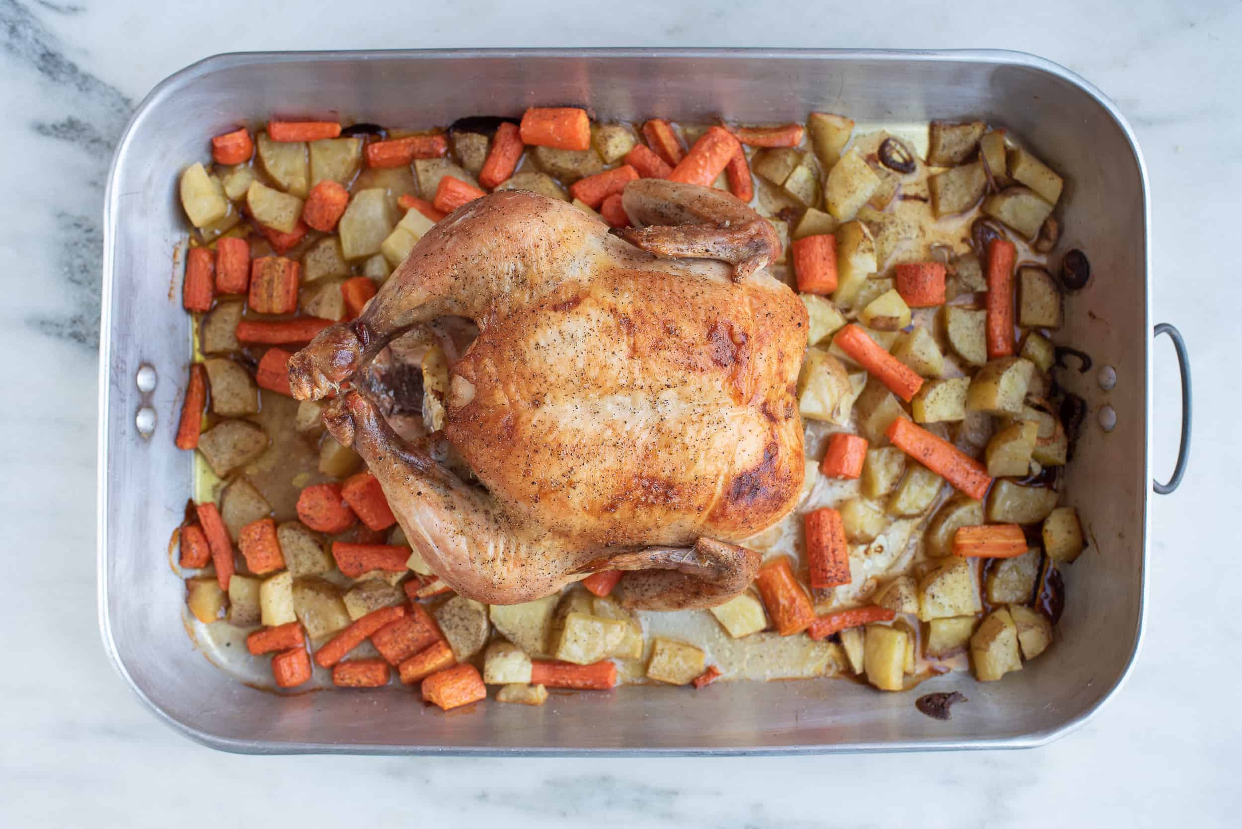 whole roasted chicken in a pan with cut up carrots and potatoes