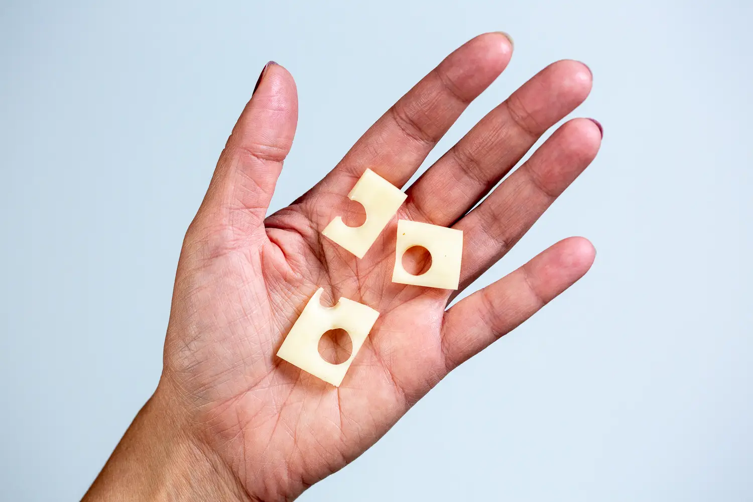 a hand holding three small bite-sized pieces of emmentaler cheese cut from a thin slice