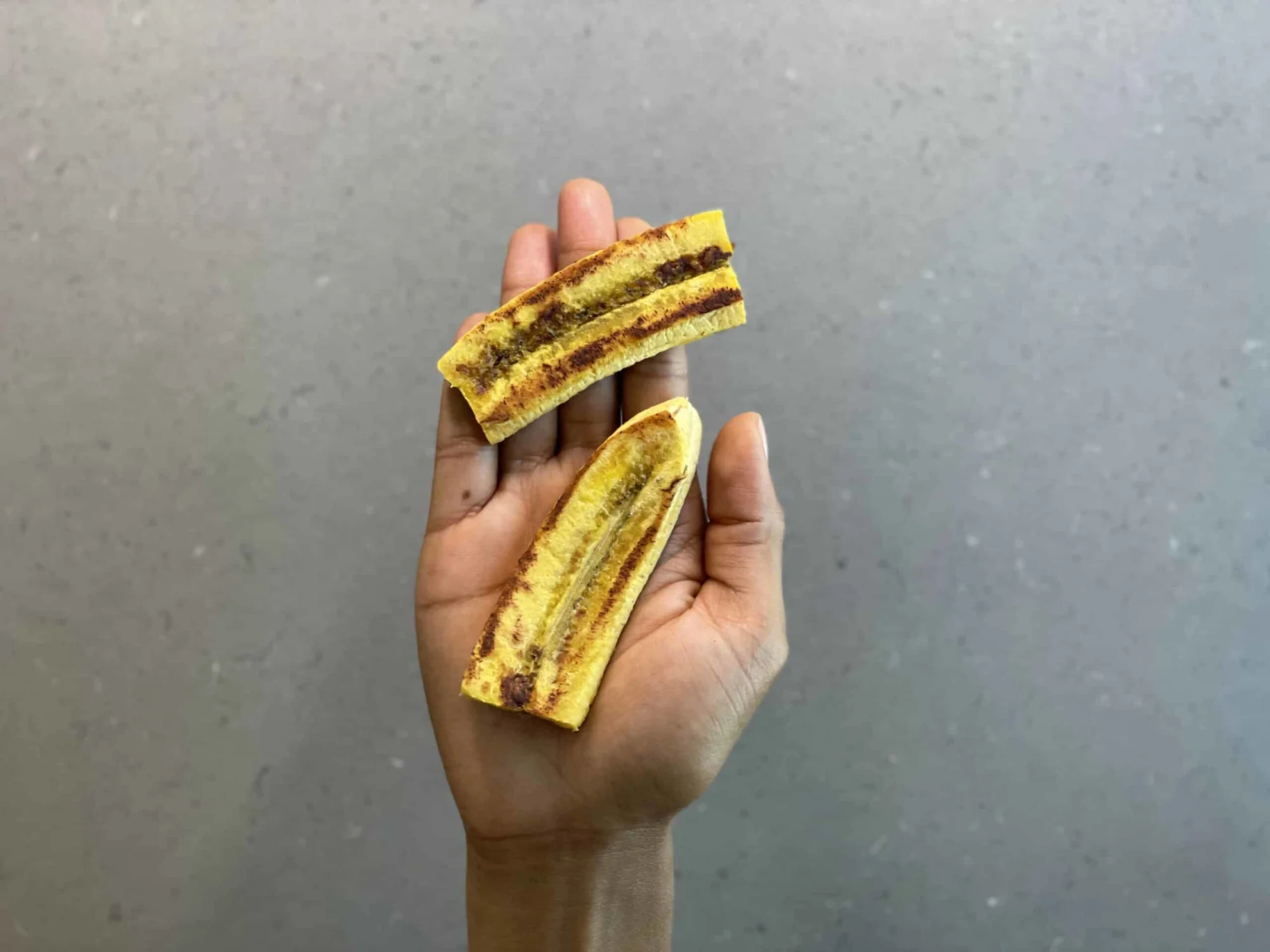 a hand holding two large, cooked pieces of plantain for babies 6 months+