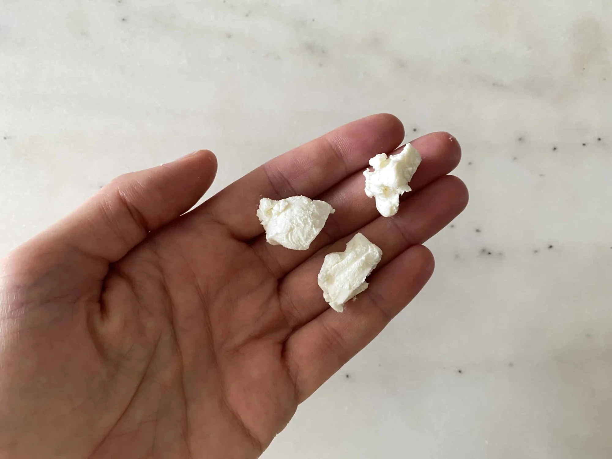 hand holding three large goat cheese crumbles