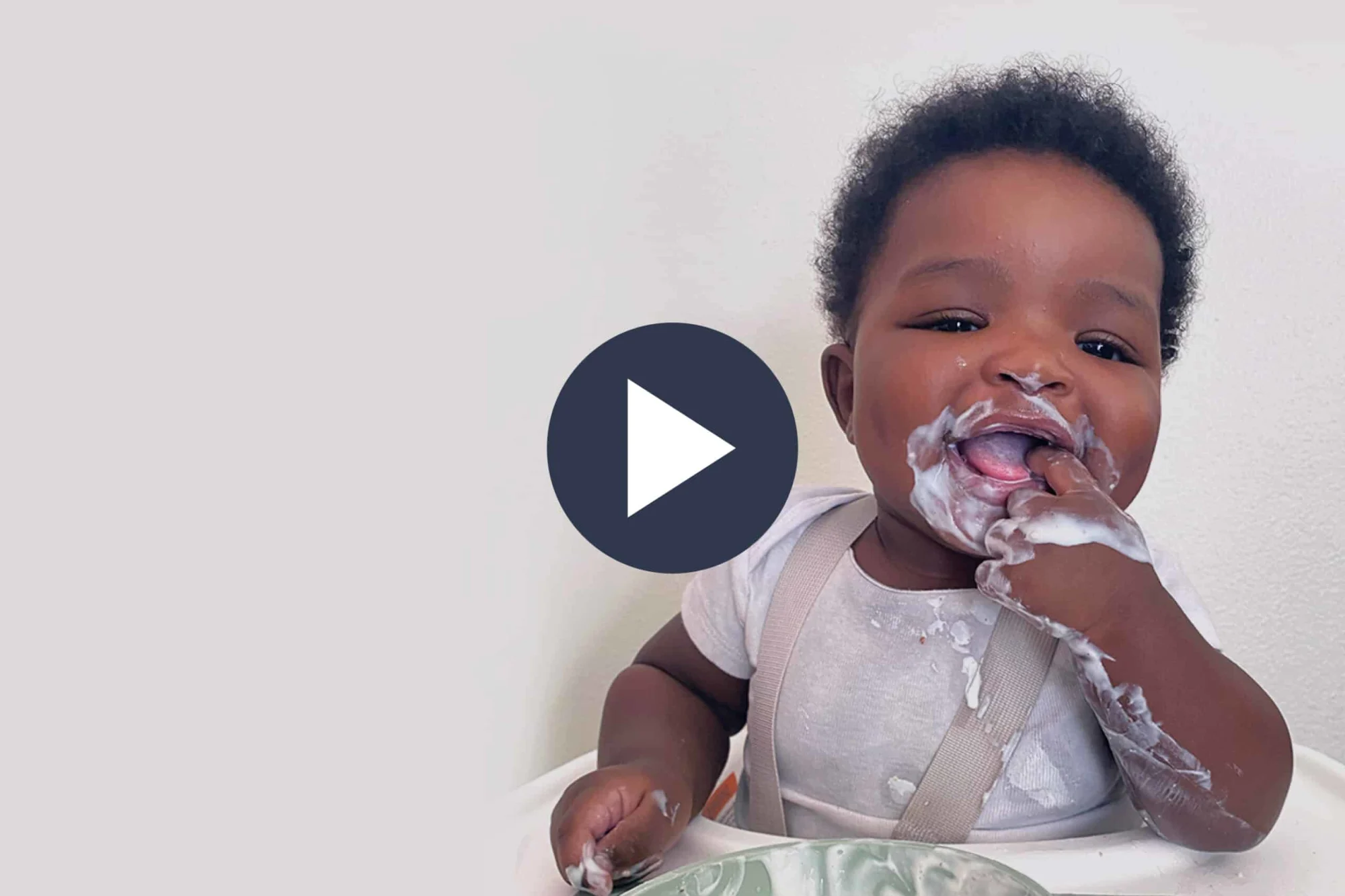 a baby sitting on a white high chair smiling with yogurt around his mouth, face and hands