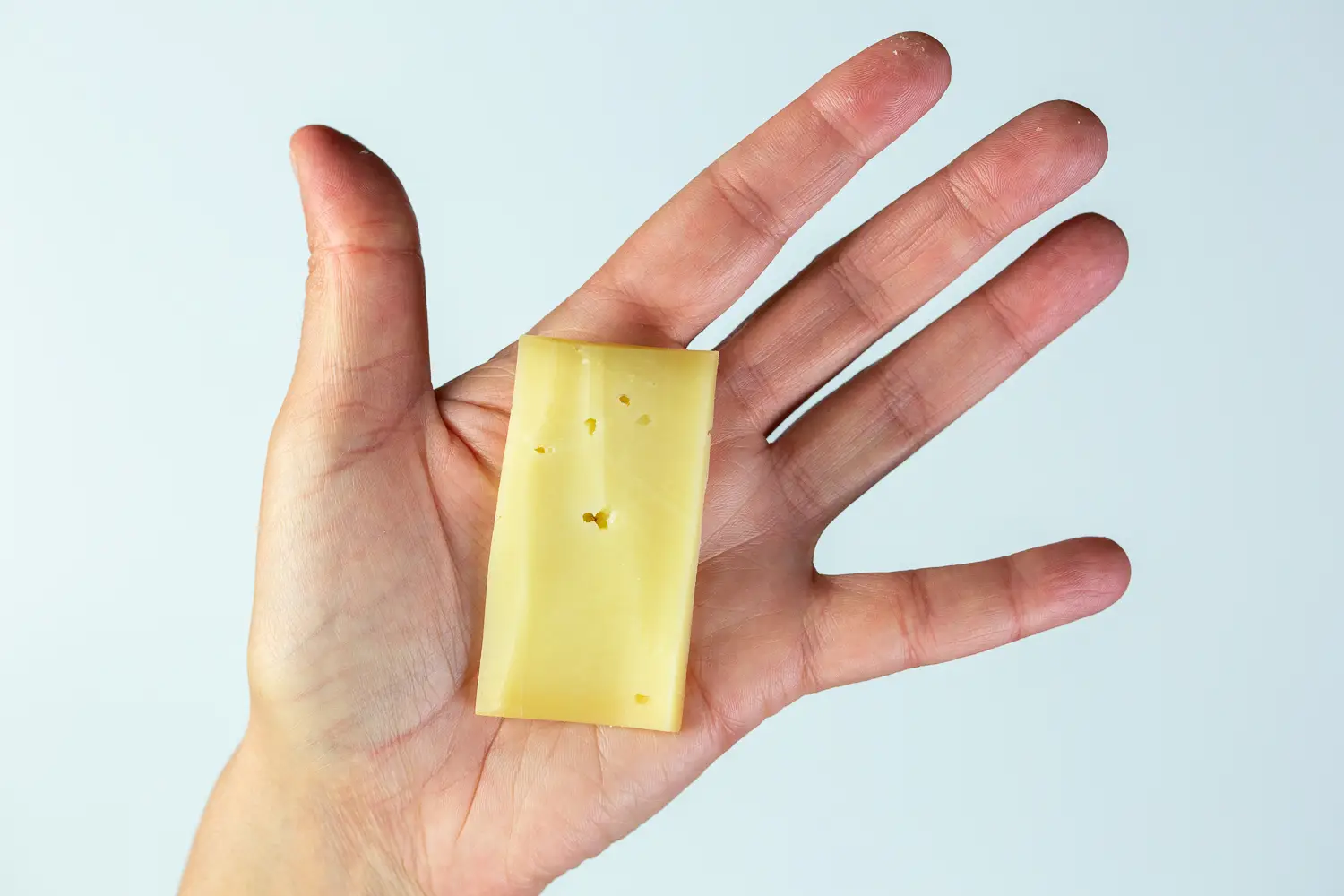 a photograph of a hand holding a long flat slice of fontina in the palm