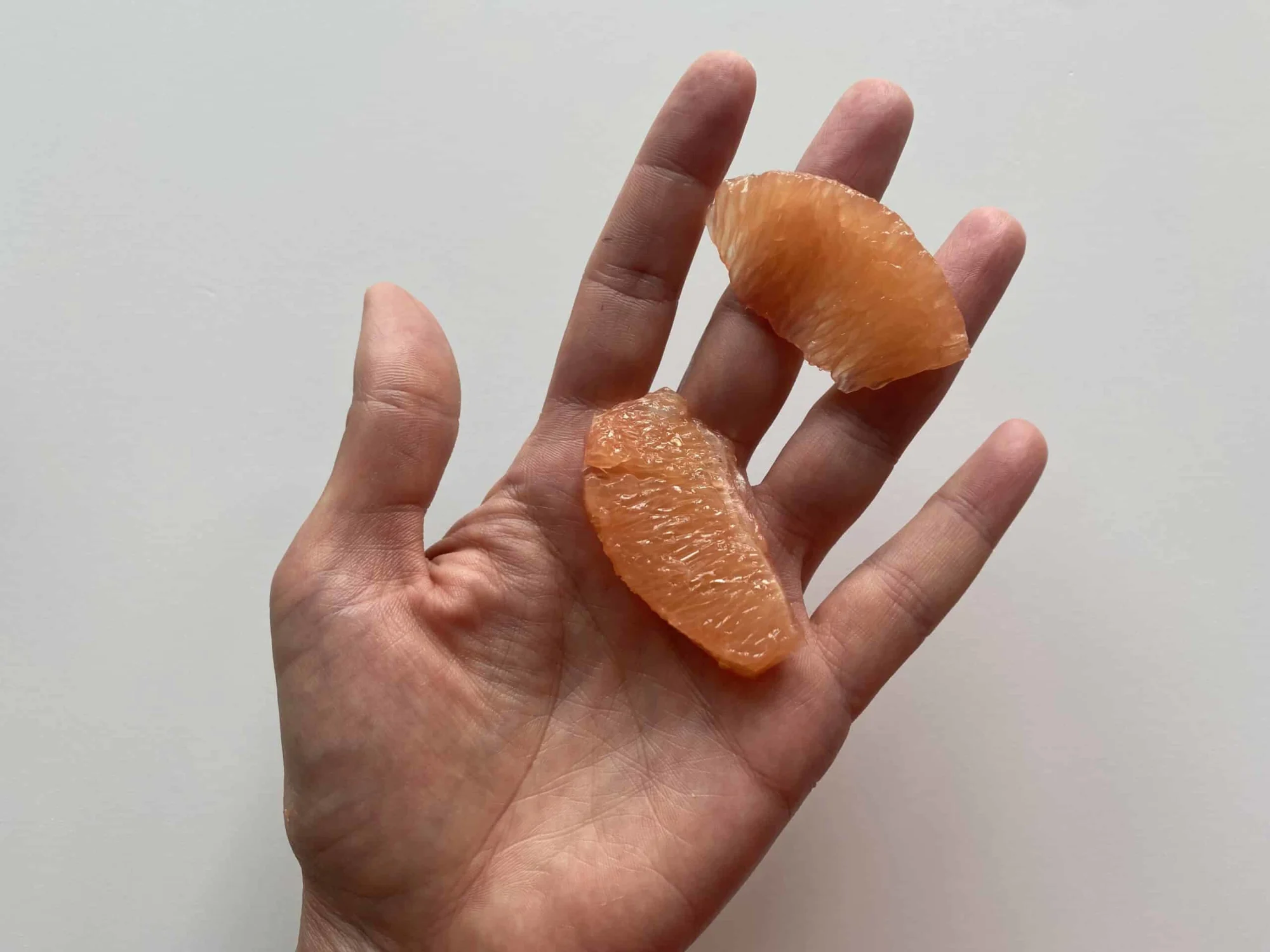a hand holding two slices of grapefruit with peel and membrane removed for babies 6 months+