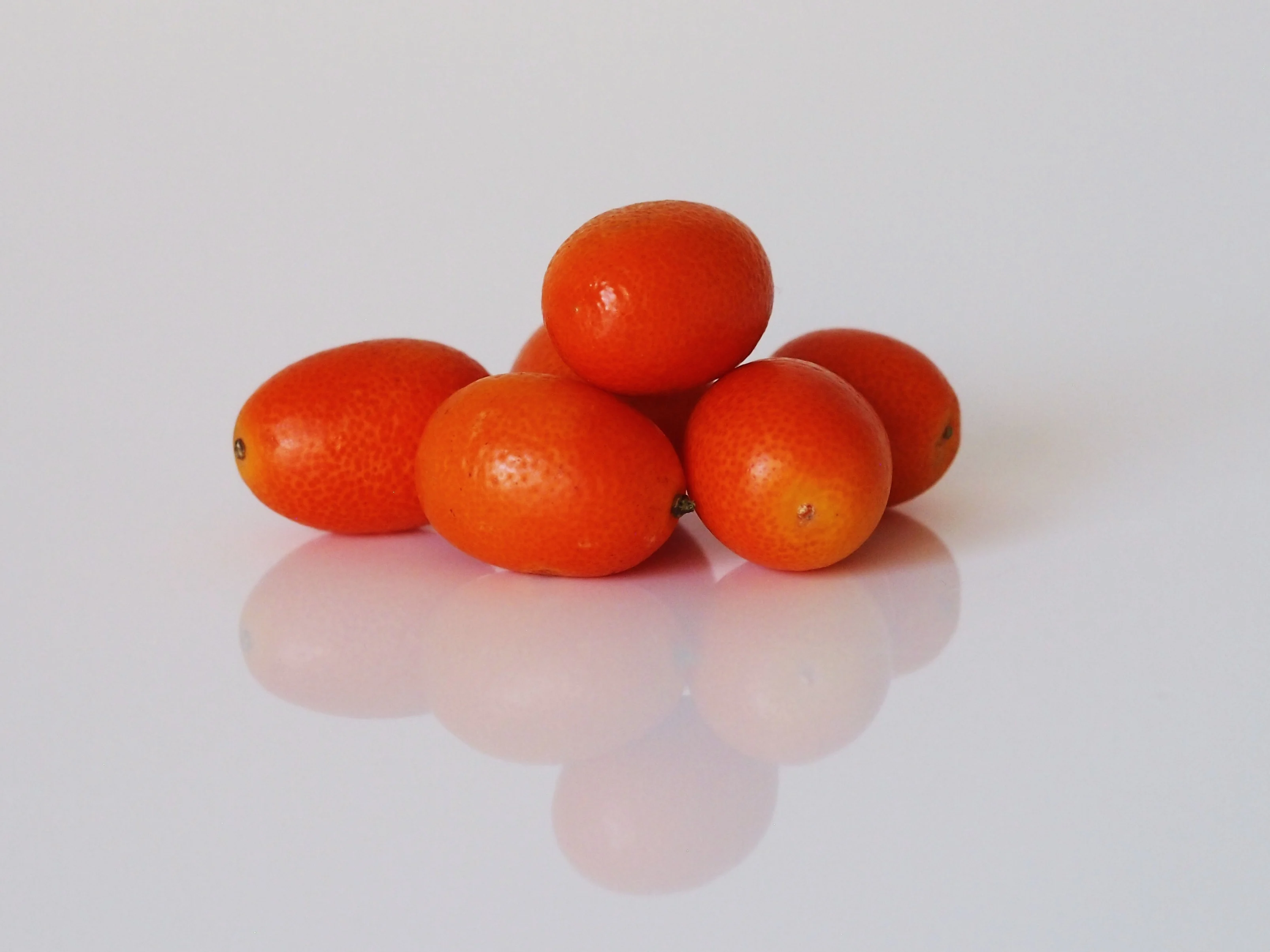 a photograph of six whole kumquats on a white background