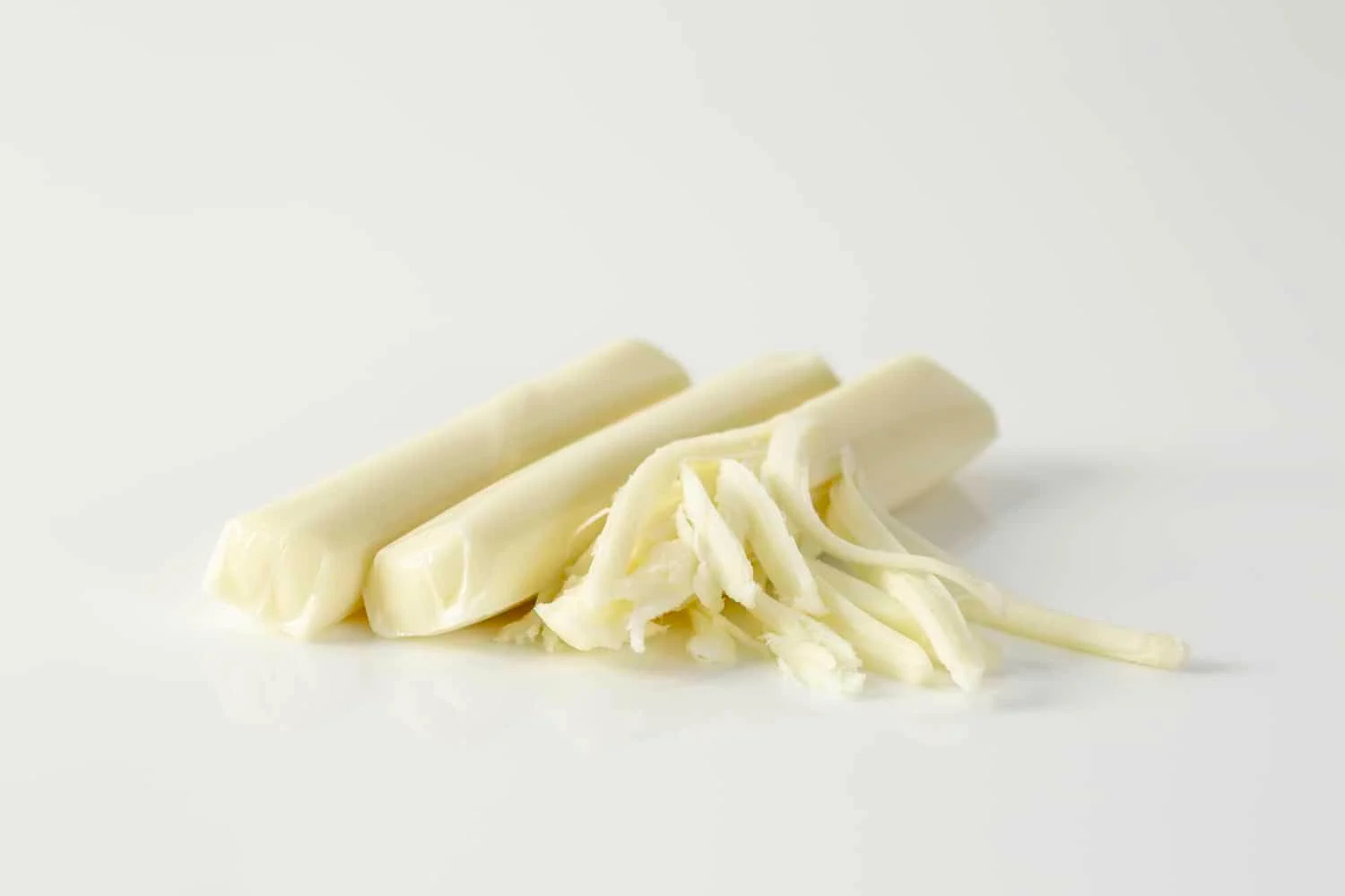 three sticks of string cheese on a white background, one of them partially pulled apart into strands