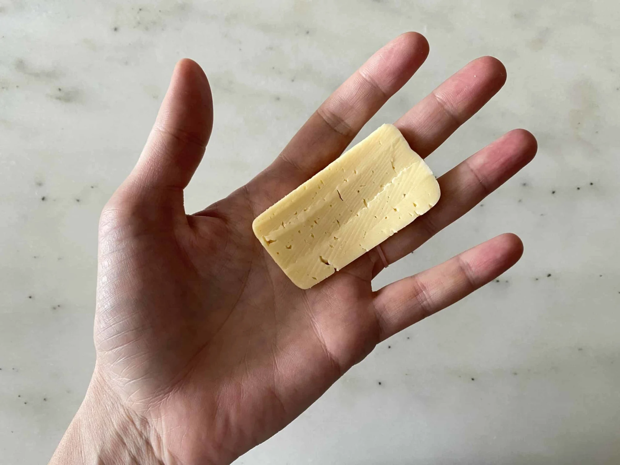 Ruler thin slice of Havarti cheese for babies on an adult hand