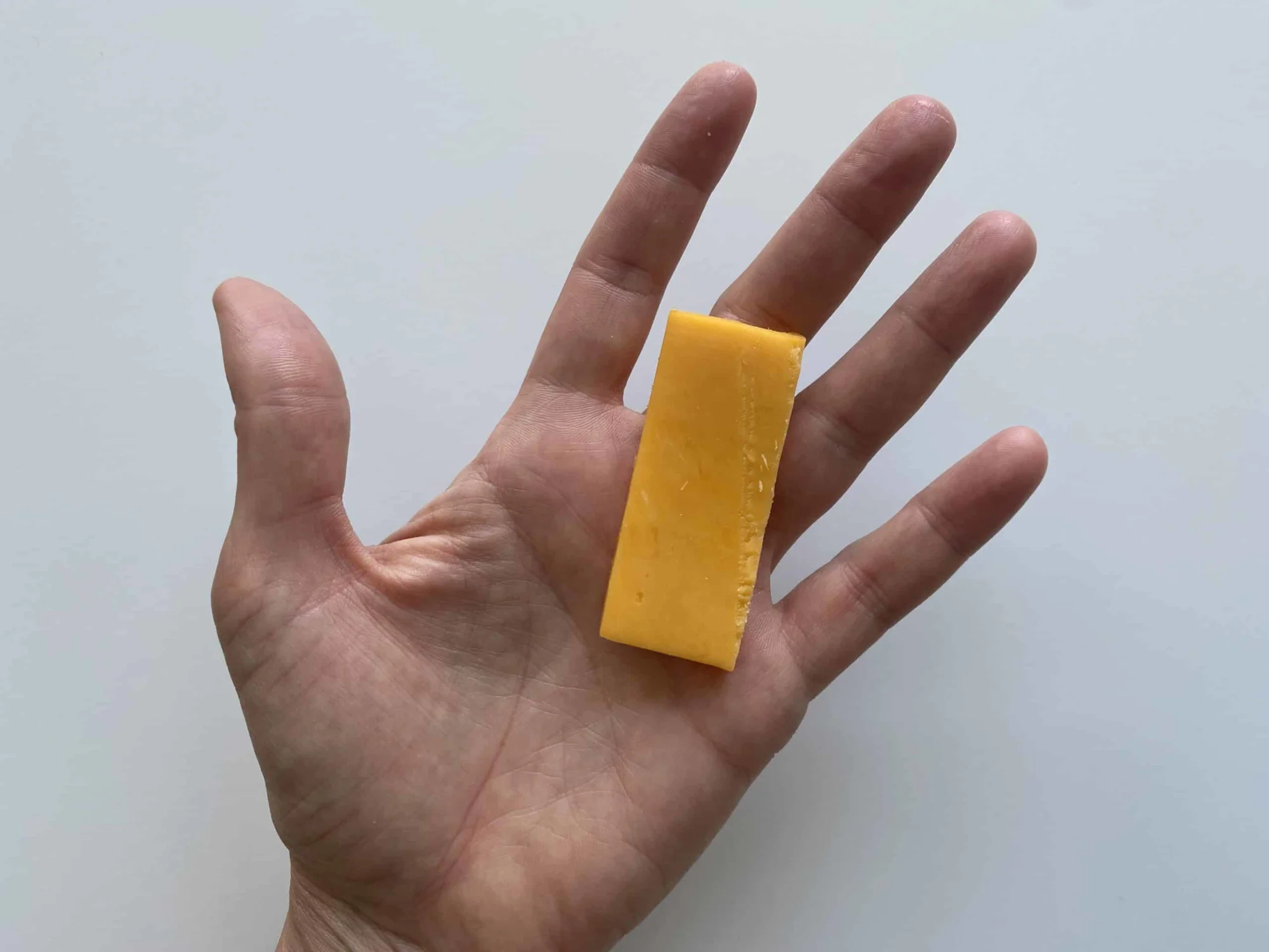 a hand holding a thin rectangular slice of colby cheese