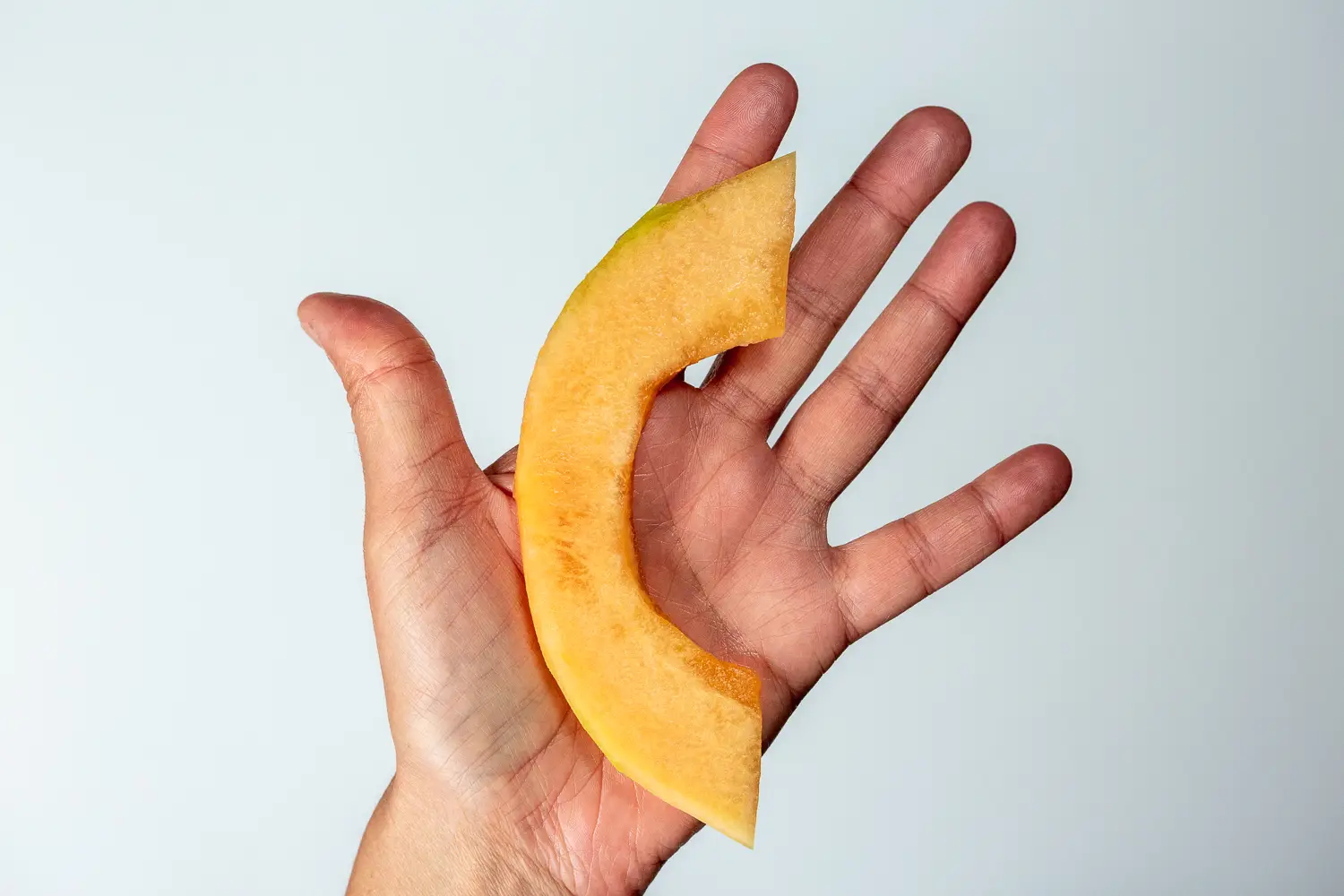 a hand holding a thin slice of cantaloupe for babies