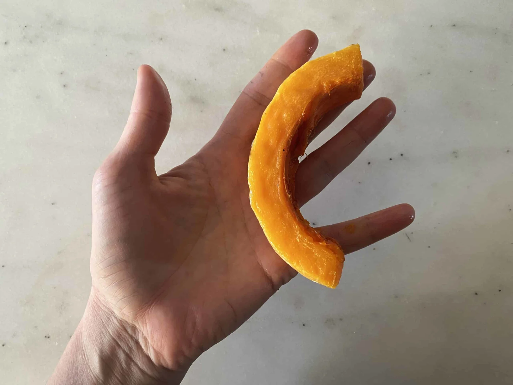 a hand holding one crescent-shaped slice of cooked peeled butternut squash for babies starting solids